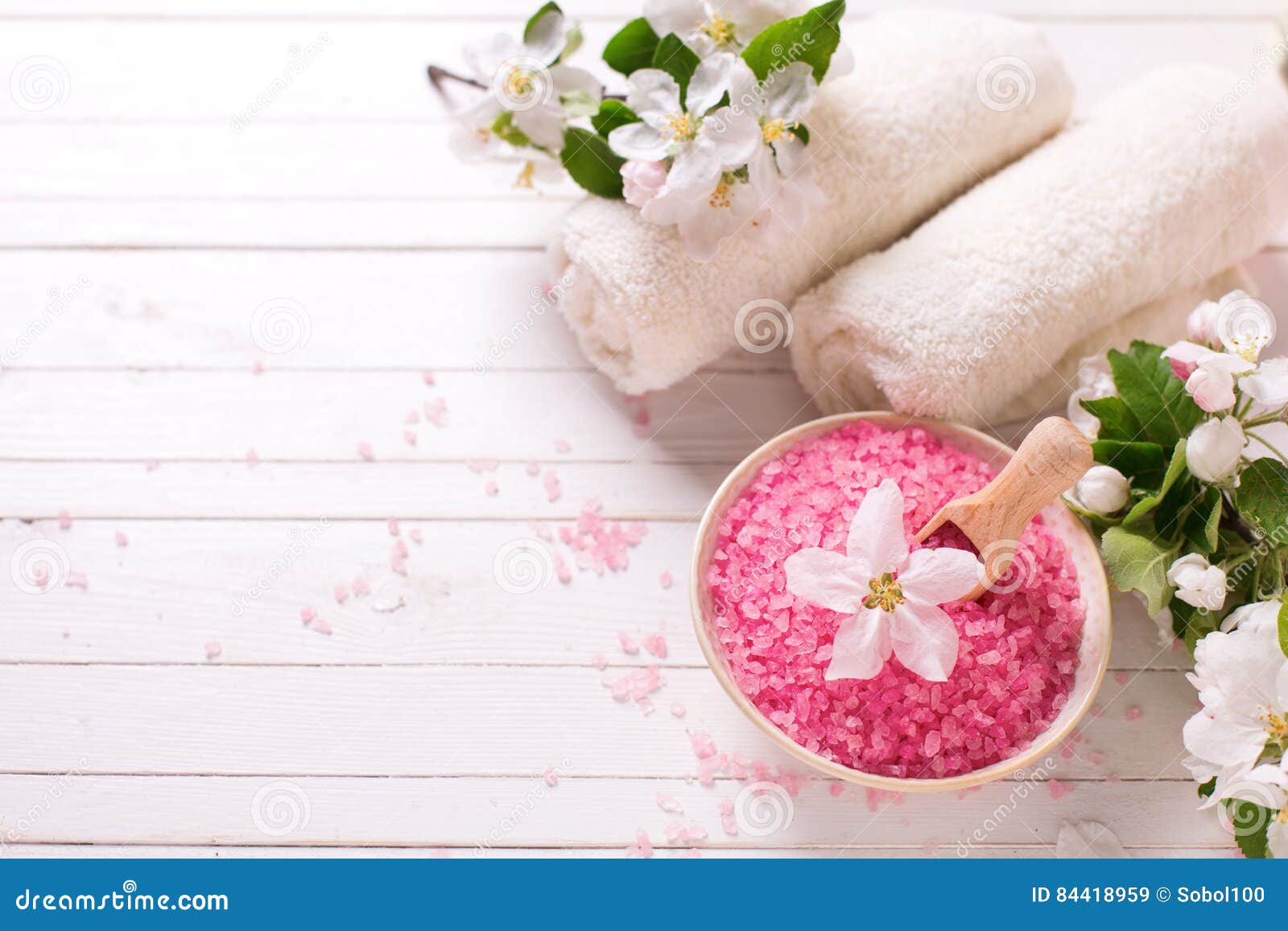 Rosa hav som är salt i bunke, handdukar och blommor på vit träbackg. Spa eller wellnessinställning Rosa hav som är salt i bunke, handdukar och blommor på vit träbakgrund Selektivt fokusera placera text