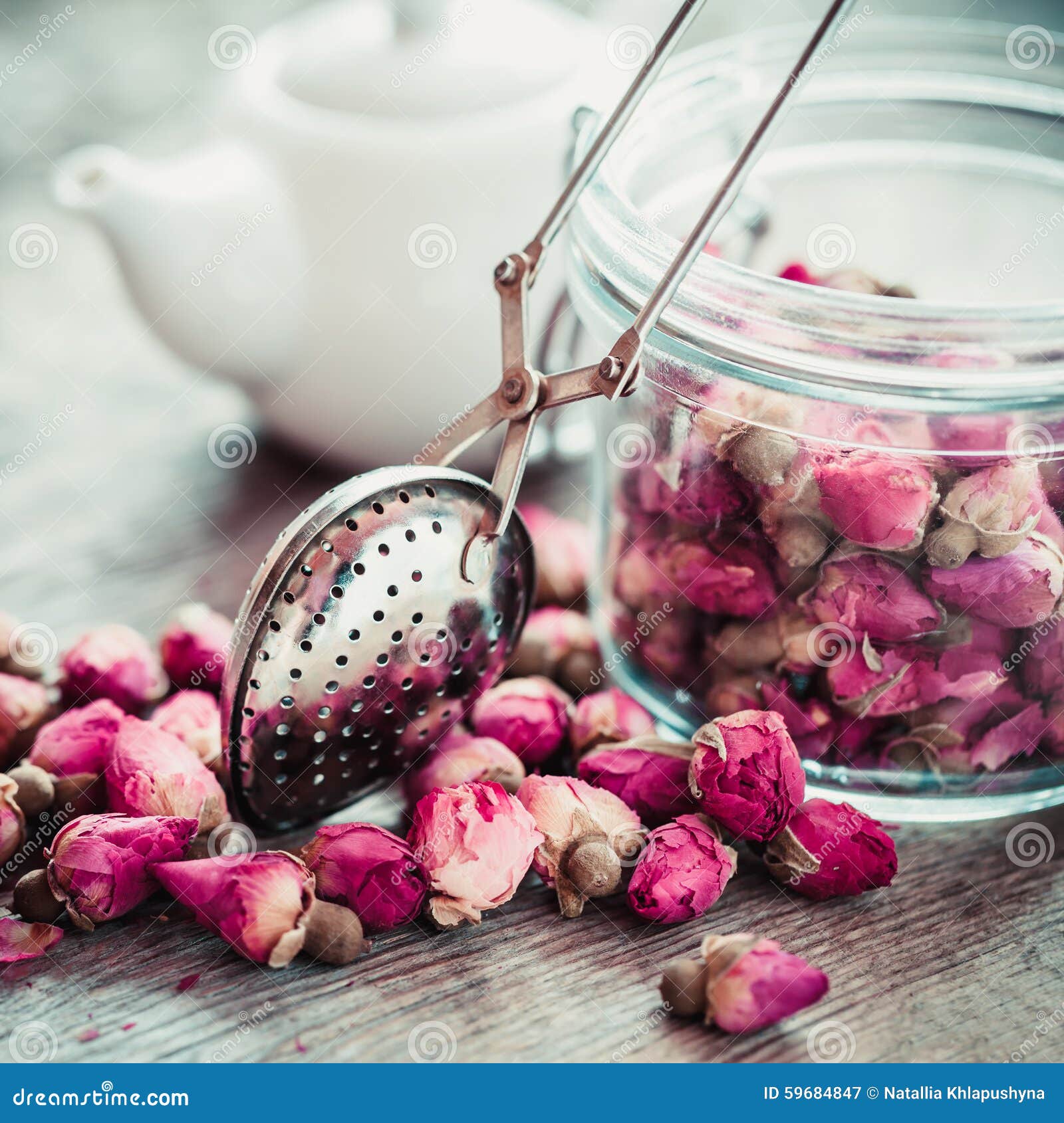rose buds tea, tea infuser, glass jar and teapot on background.