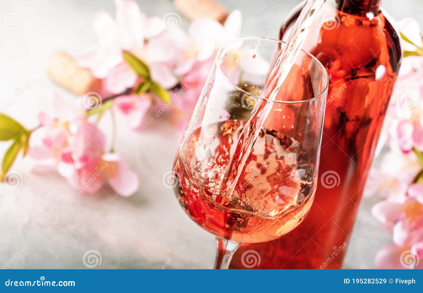 rose wine pouring out of the bottle, gray bakcground, pink flowers. rosado, rosato or blush wine tasting in wineshop, bar concept