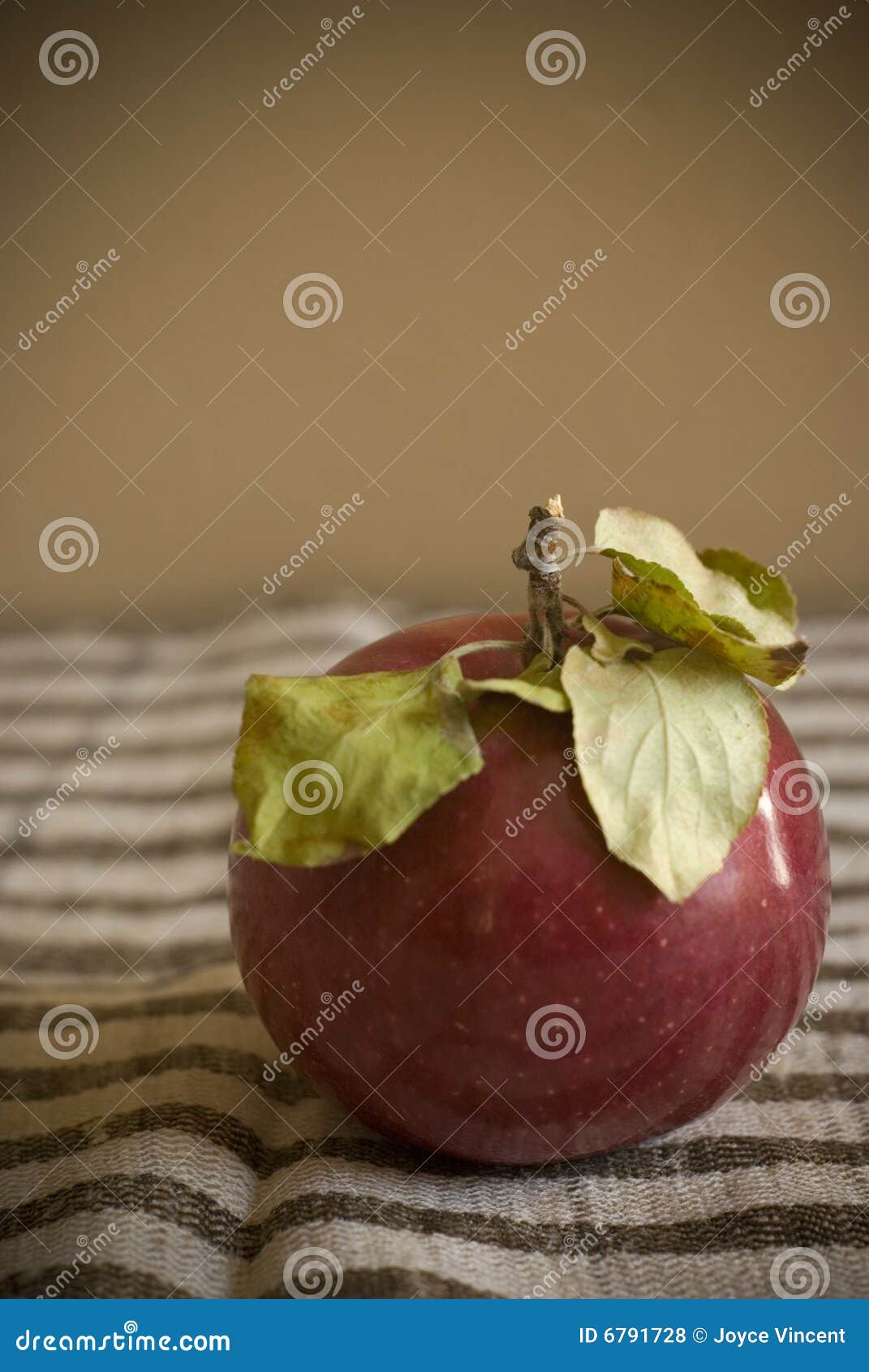 Ein roter Apfel mit Grün verlässt auf einem Braun und Tan einer striped Matte und einem tan Hintergrund.