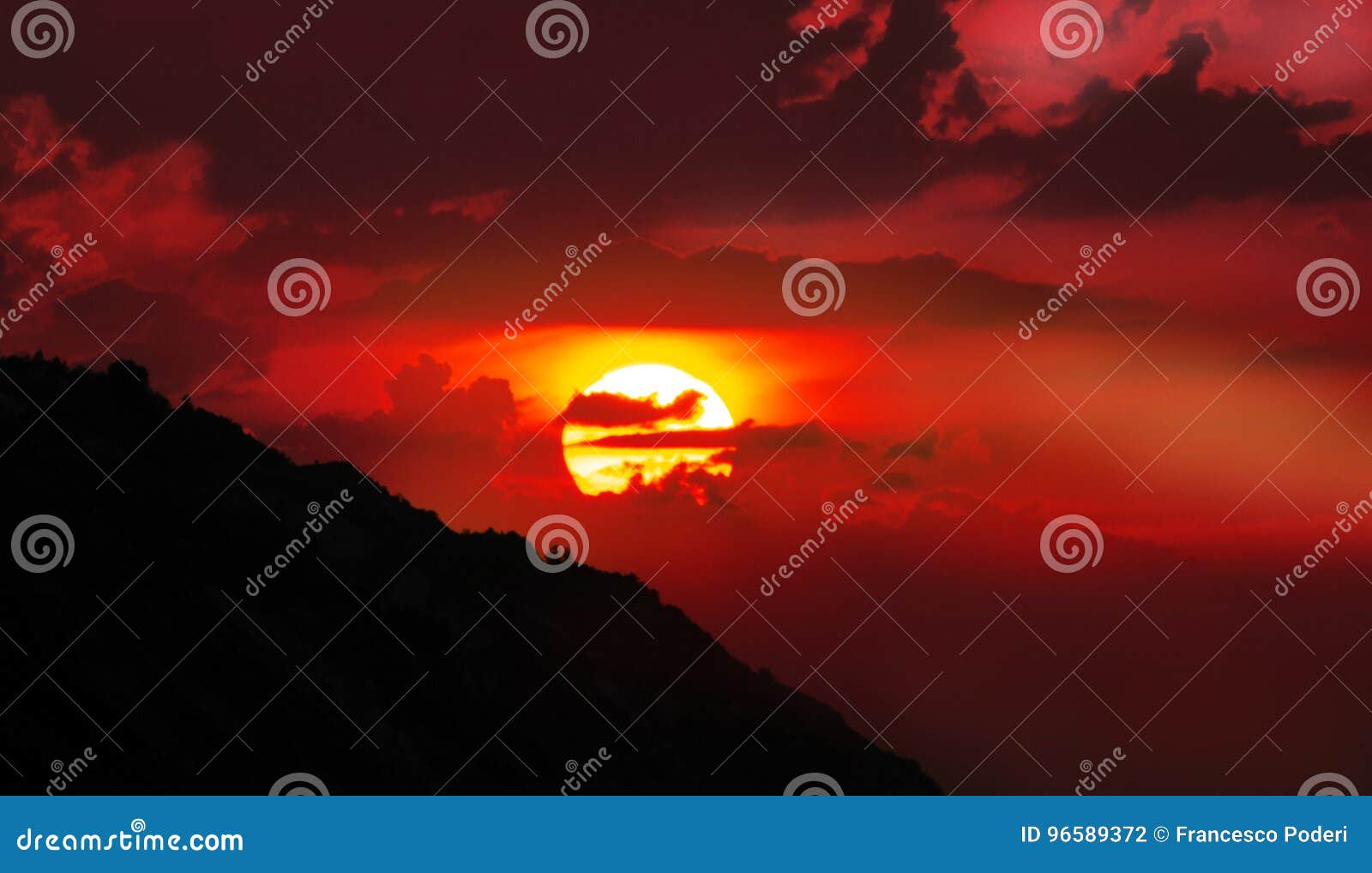 Roter Sonnenuntergang. Solche intensive rote Sonneneinstellung durch das Meer über einem Hügel mit rötlichen Wolken um ihn