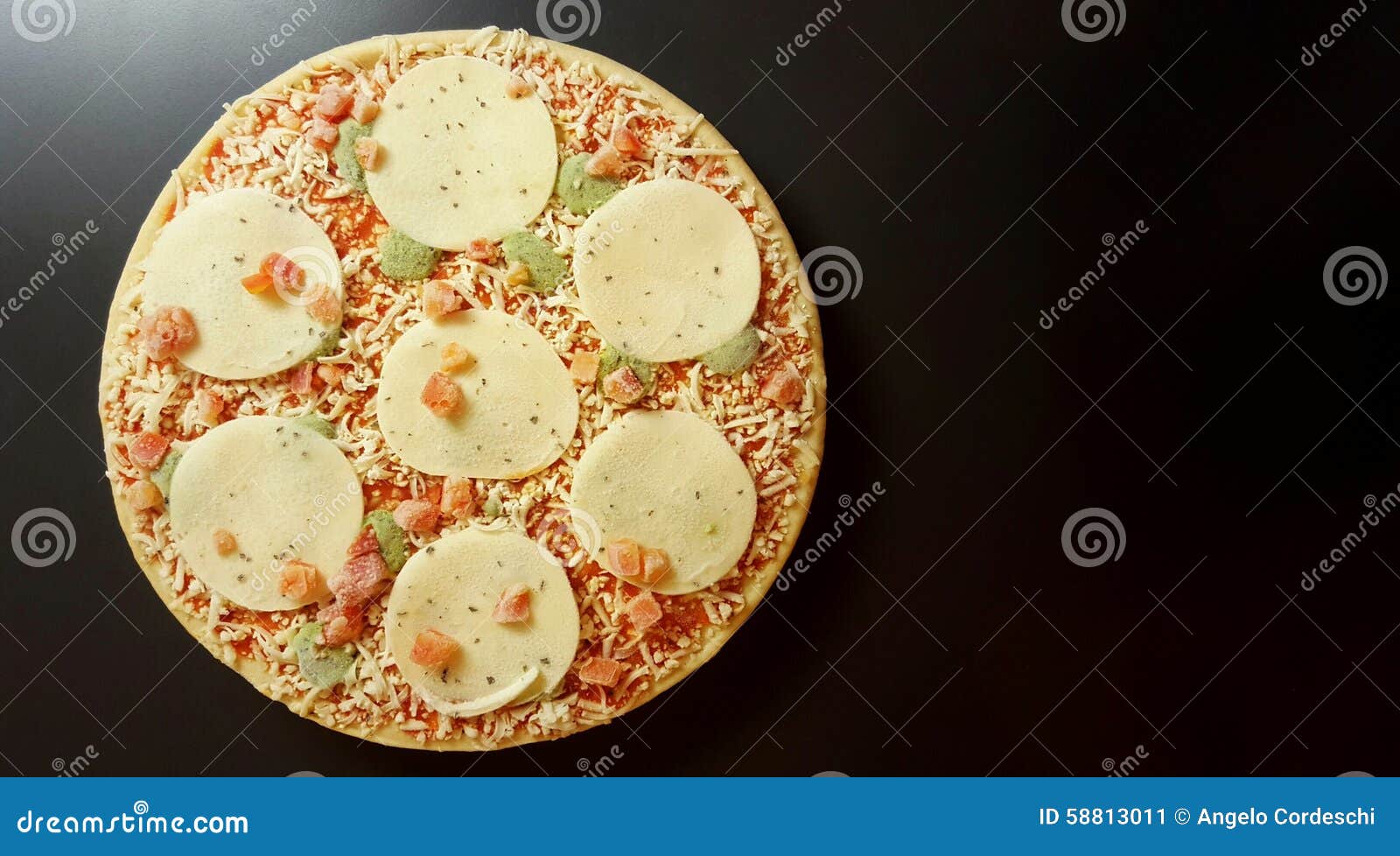 round frozen pizza. tomatoes, mozzarella, pesto, basil. anthracite background.