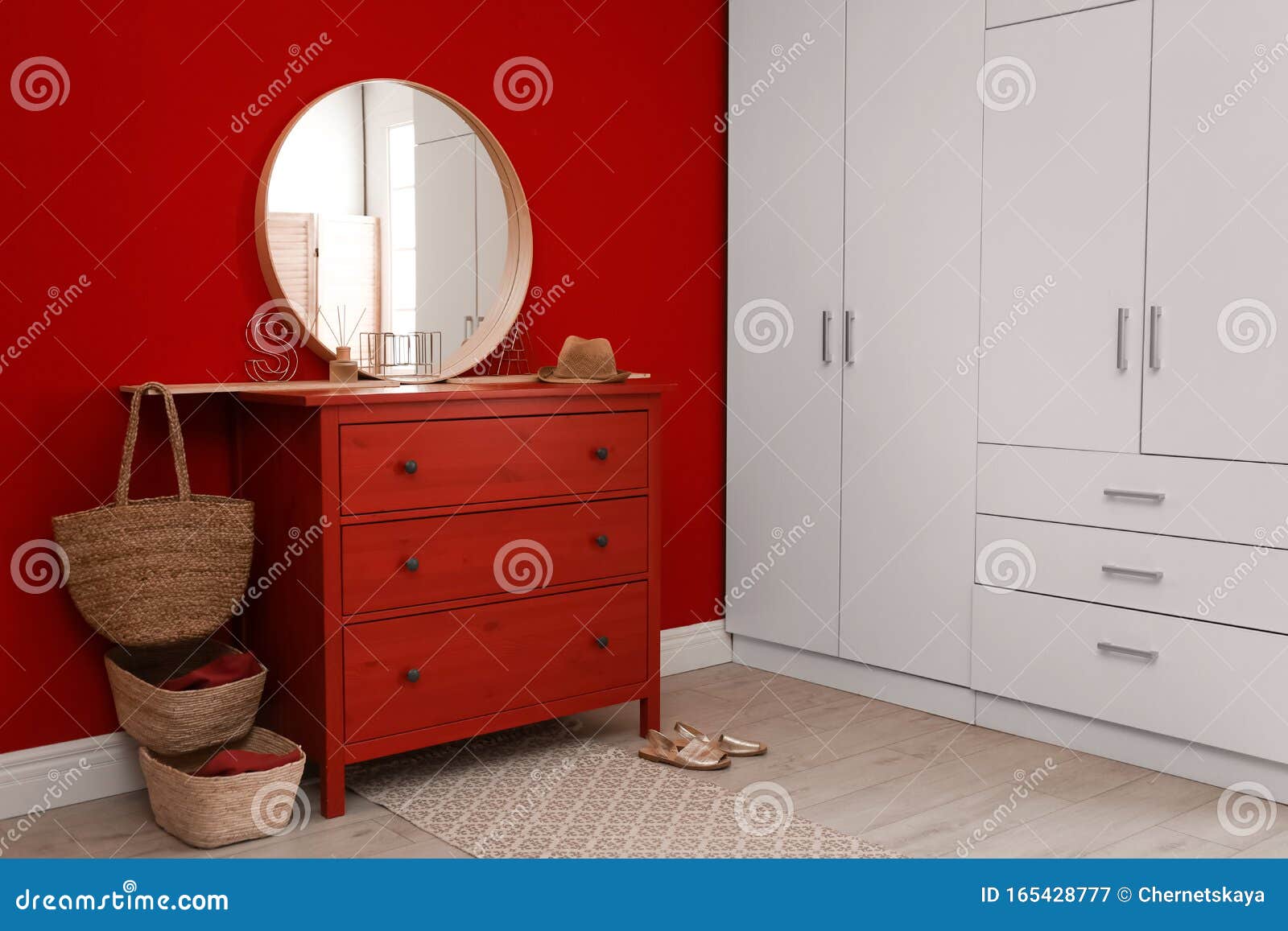 Round Mirror And Chest Of Drawers Near Red Wall In Room Stock