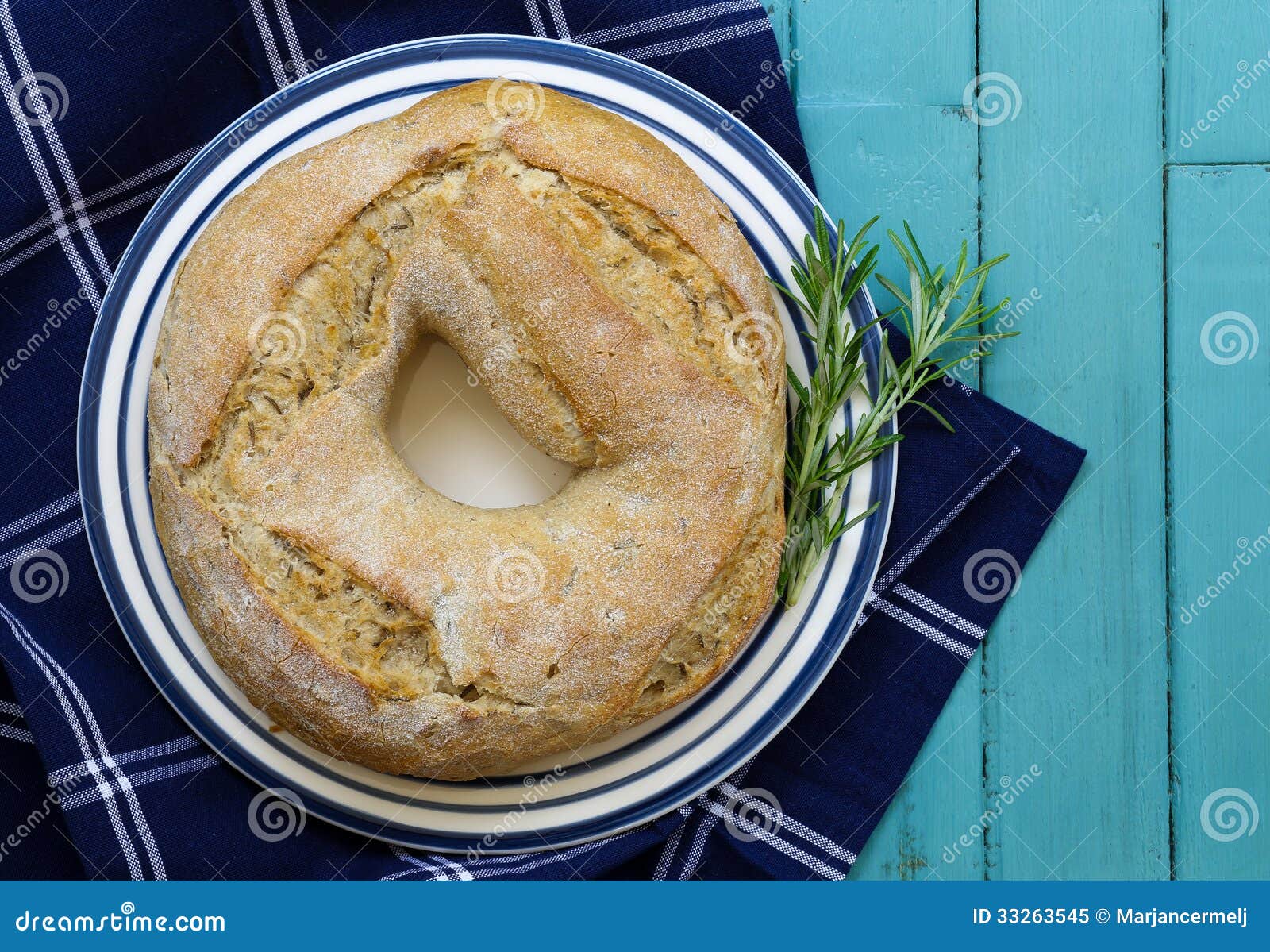 Round Potato Rosemary Bread With Hole on plate with blue stripes, rosemary branch, dark blue table cloth and rustic turquoise table