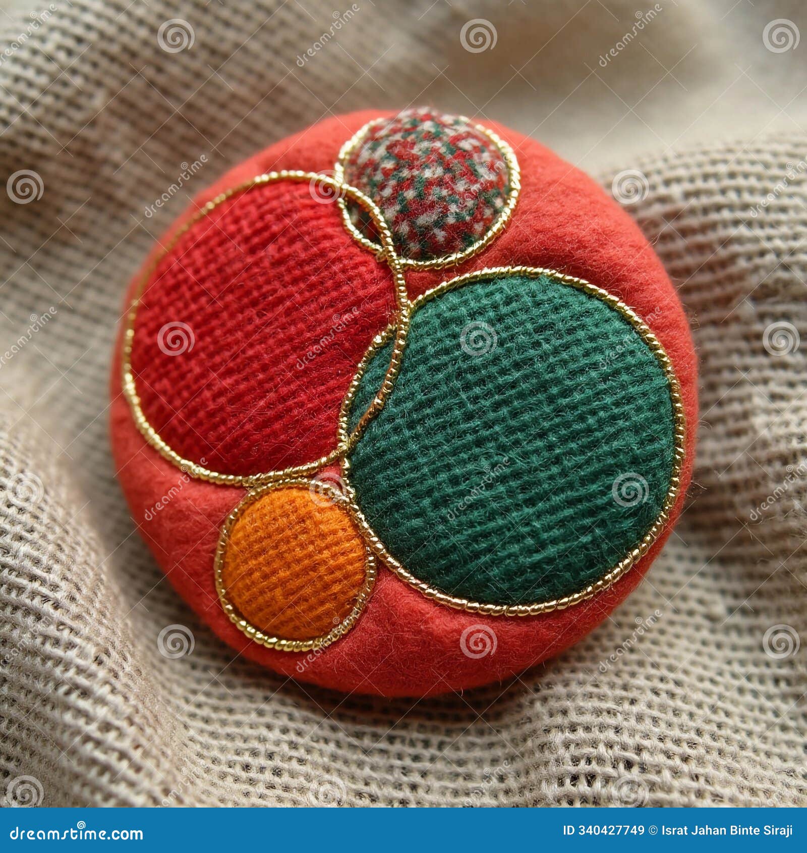 a round textile badge featuring abstract geometric s in red, green, and orange, separated by fine golden threads, placed on a
