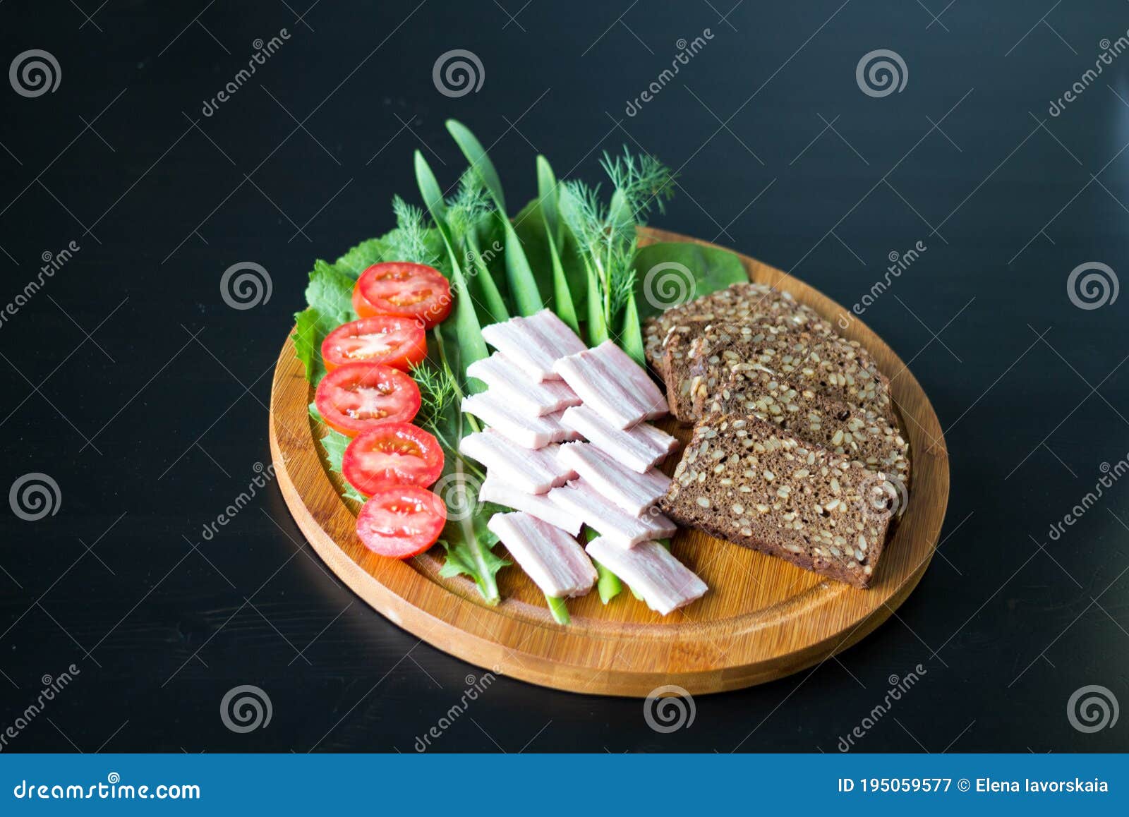 on a round wooden board is sliced black bread with seeds, smoked brisket, green onions, lettuce, tomatoes and dill. black