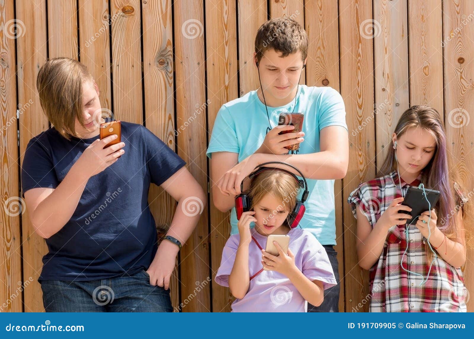 row of four friends using cellular phones. children and gadget concept.