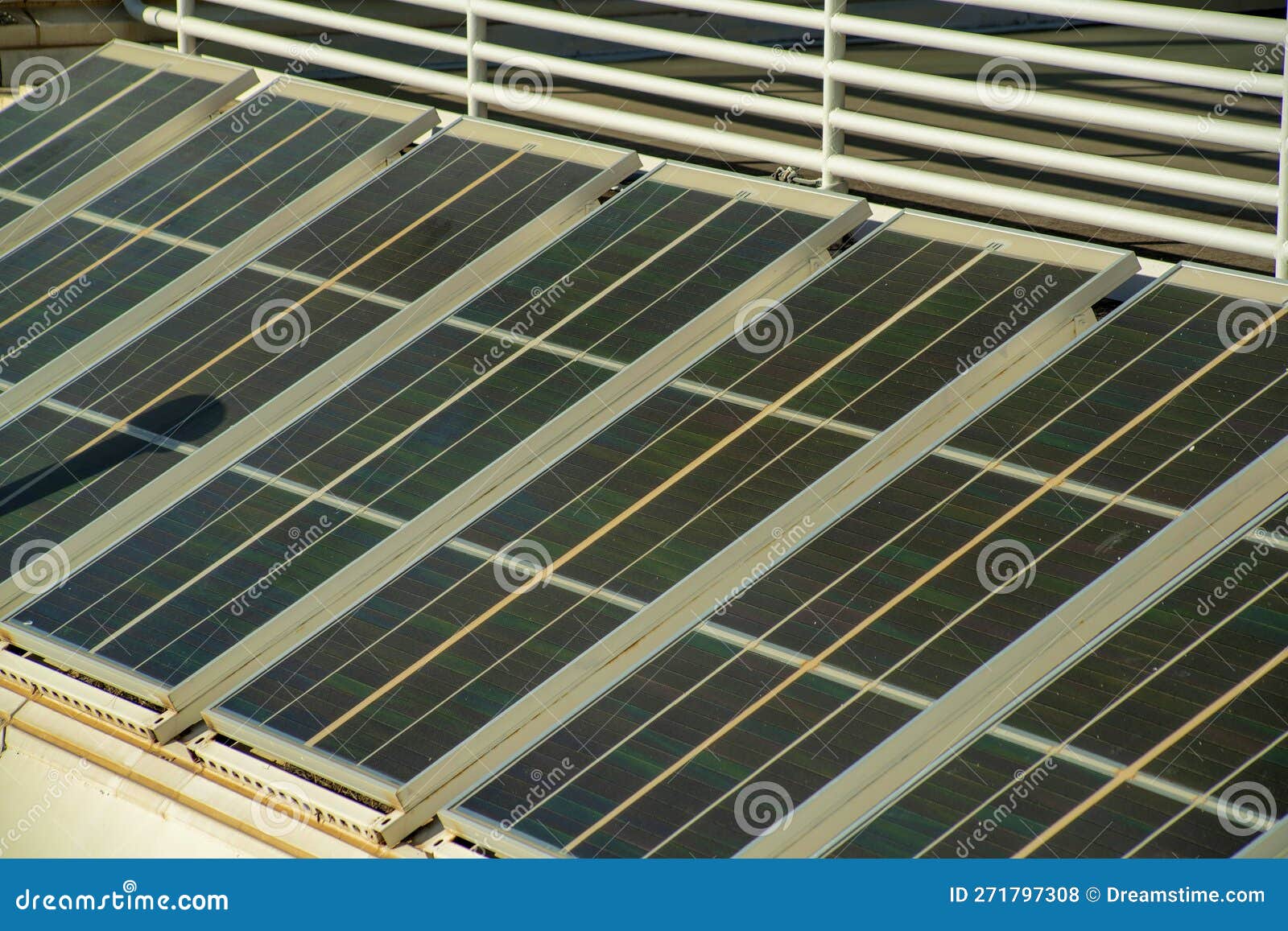 row of industrial photovoltaic or solar pannels on side of building with metal gaurd rail at thirty degree angle for sun
