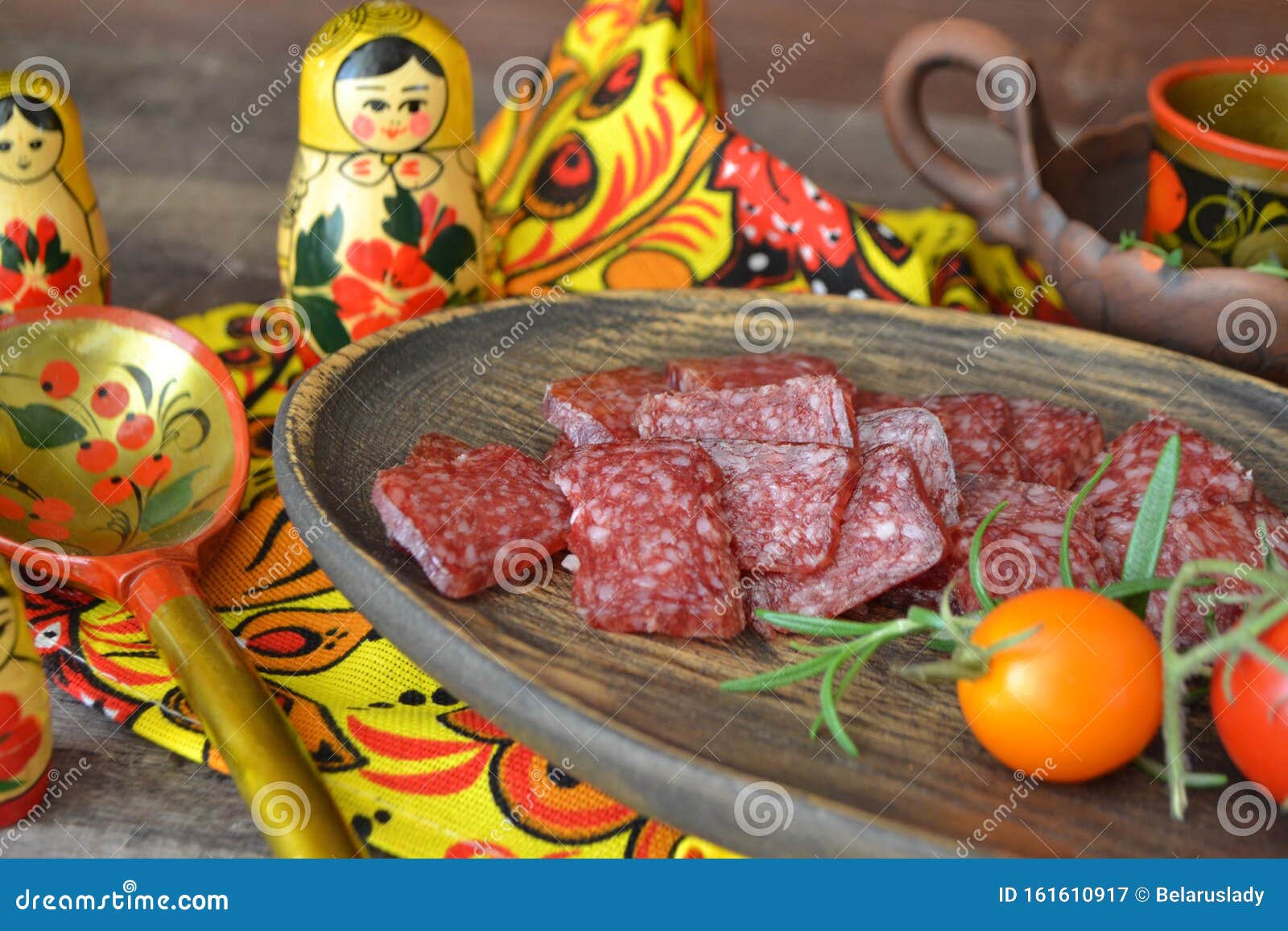 russian salami sausages sliced on rustic wooden plate, bright matroshka dolls, spoon khokhloma