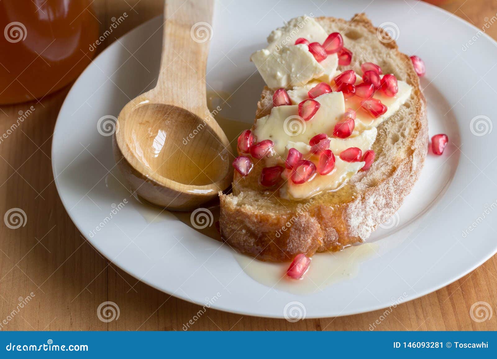 rustic bread slice with cheese, pomegranate seeds and honey on plate close up