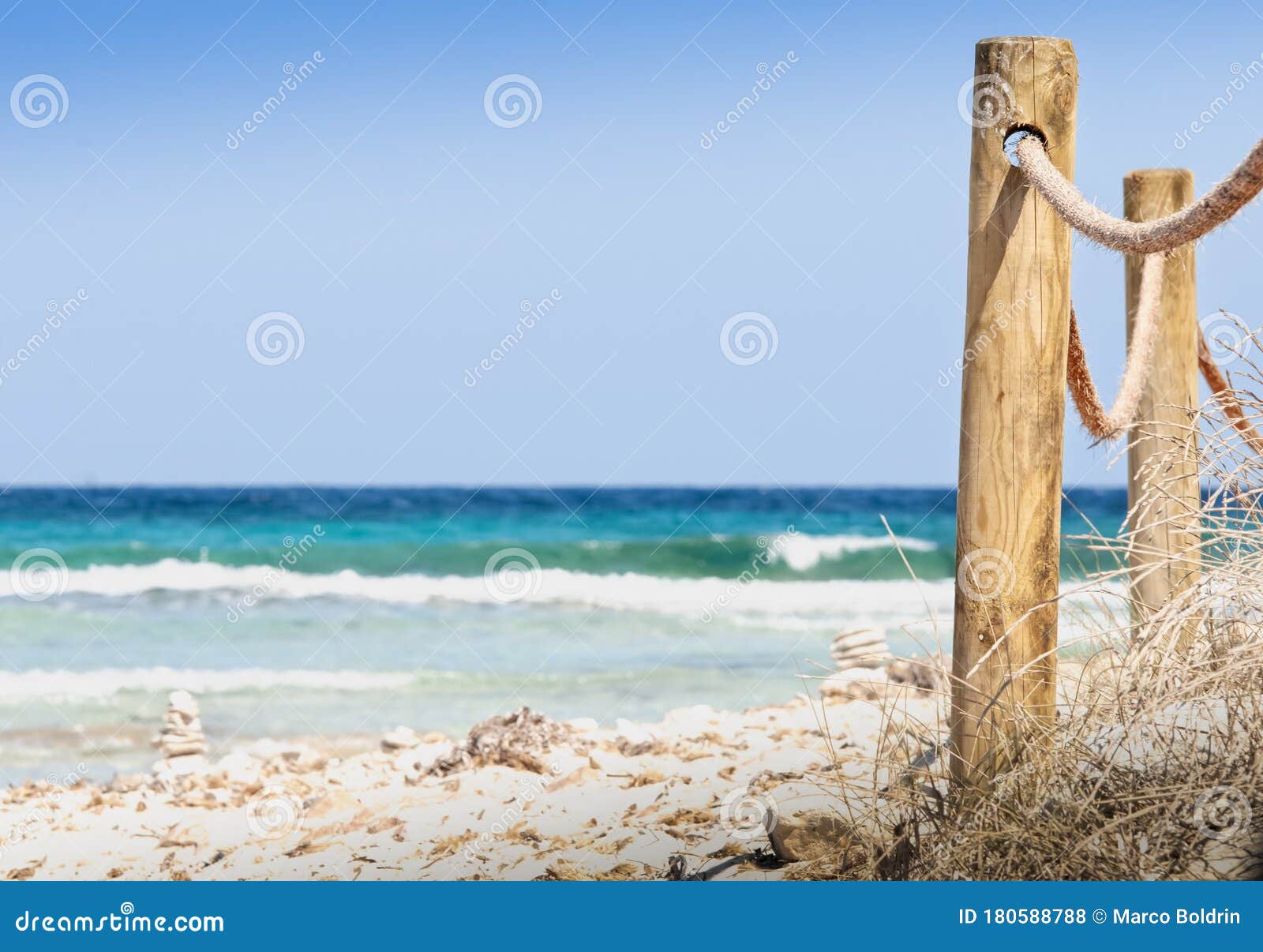 rustic fence with wooden poles and rope on a deserted beach, in the background the rough sea