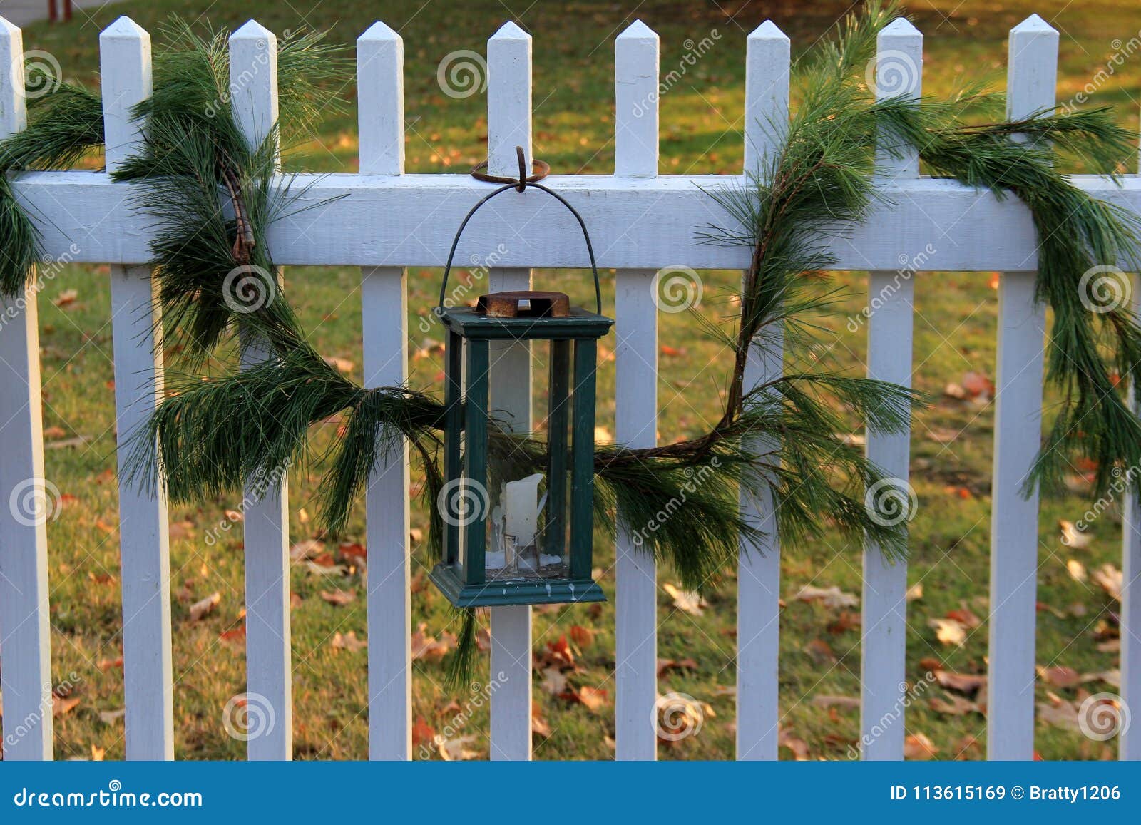 Inviting scene with white picket fence green boughs from fir tree and lantern as Christmas decoration that wel es guests in for a visit