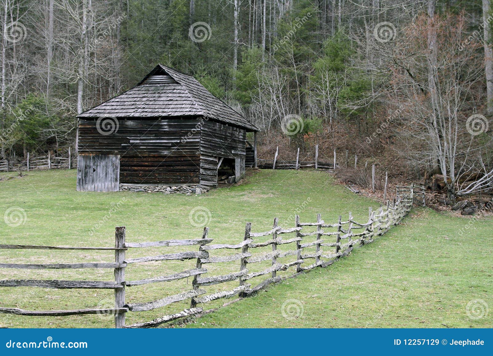 Een rustieke schuur en een houten omheining dichtbij bos