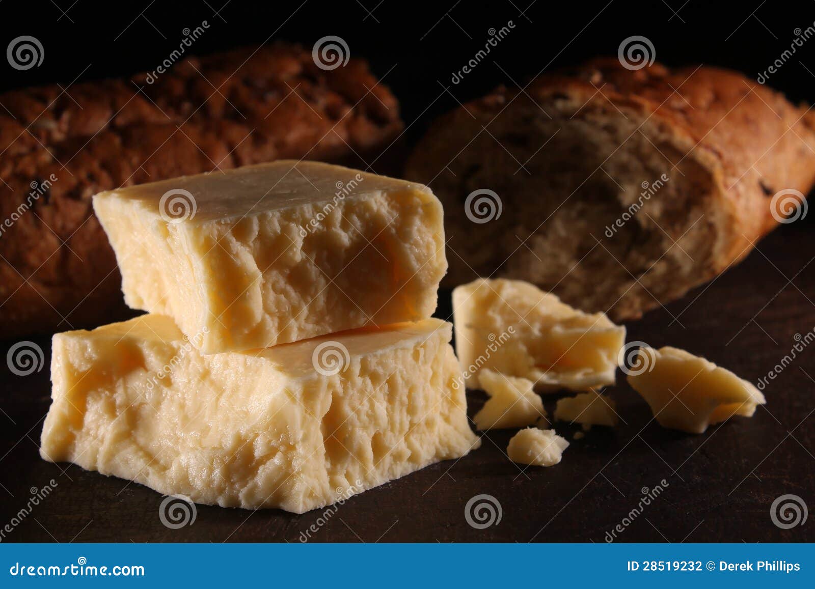 Rustikaler reifer Cheddar-Käse und Brot. Reifer Cheddar-Käse der rustikalen Art auf einem hölzernen Vorstand mit einem dunklen Hintergrund. Brown, Getreidespeicherartbrot im Hintergrund.