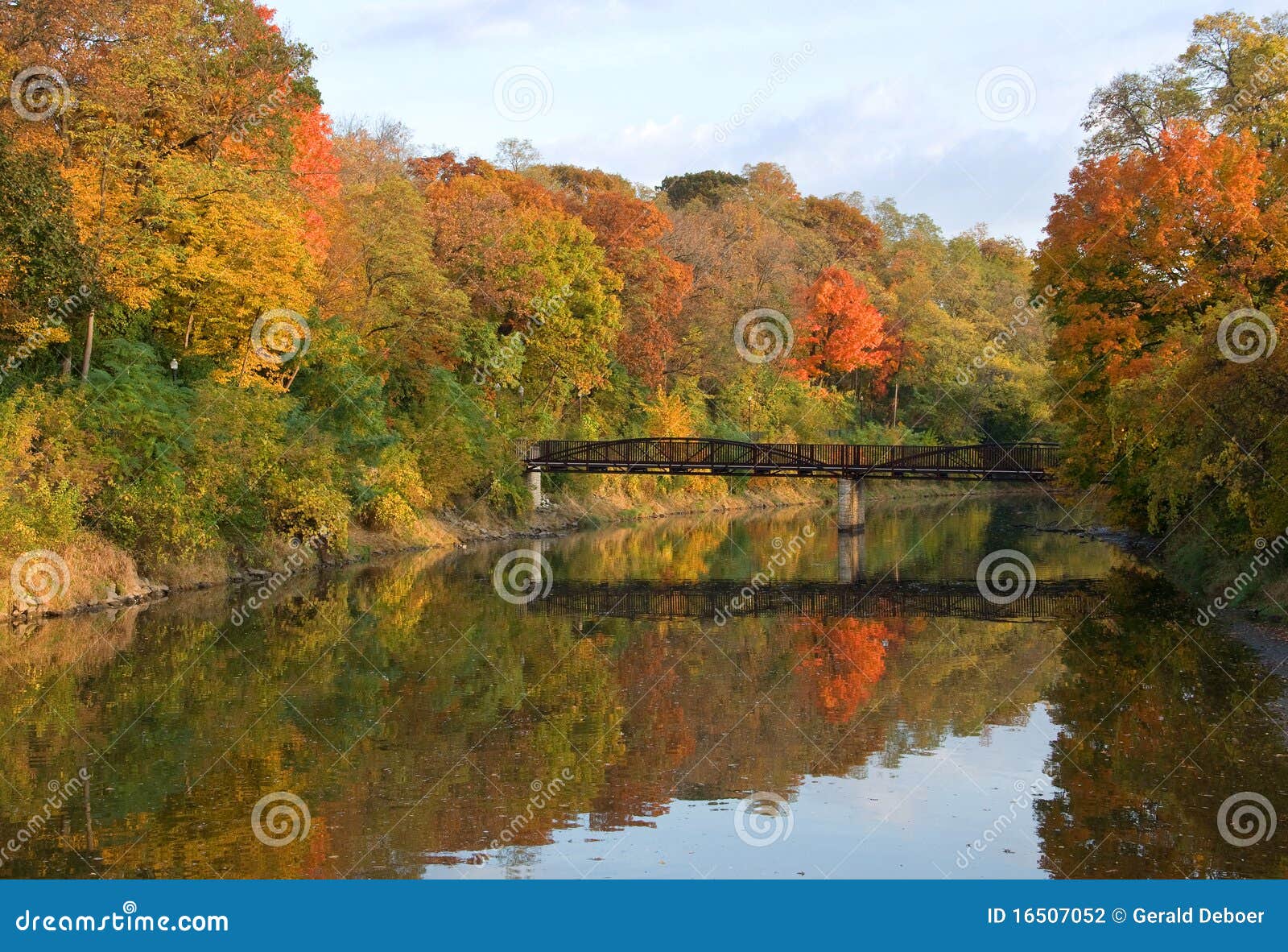 Río del otoño. La fotografía de los colores del otoño reflejó en un río de movimiento lento con una travesía interesante del puente del pie. Admitido la luz de la madrugada.