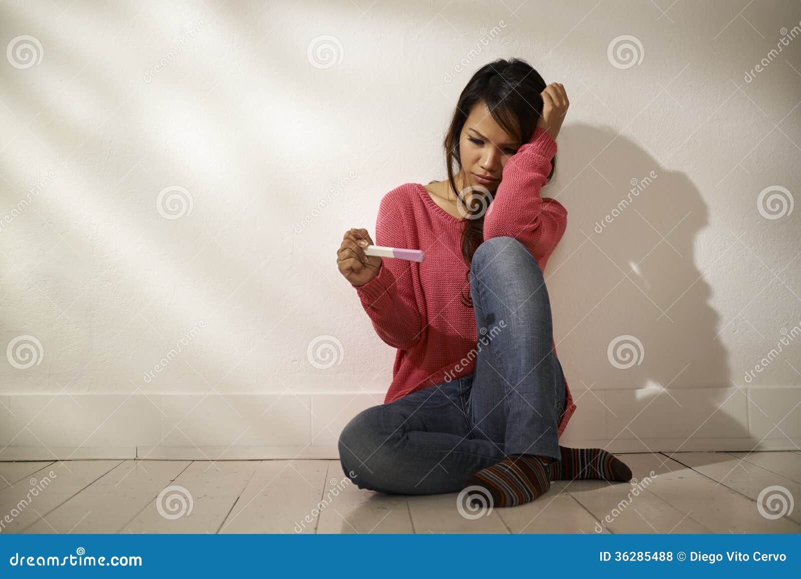 sad asian girl looking at pregnancy test sitting on floor