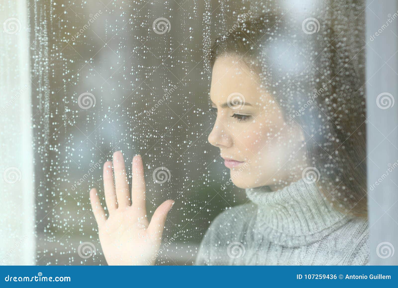 sad girl looking through a window in a rainy day