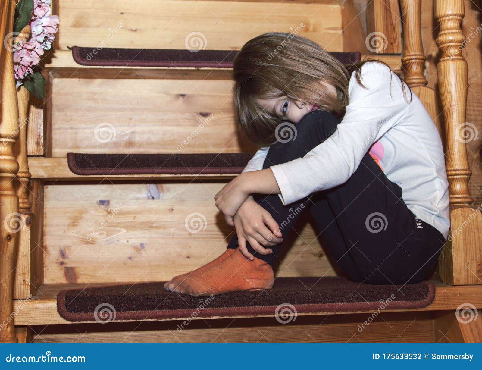 Sad Little Girl is Sitting on the Stairs with Her Knees Clasped and Her ...