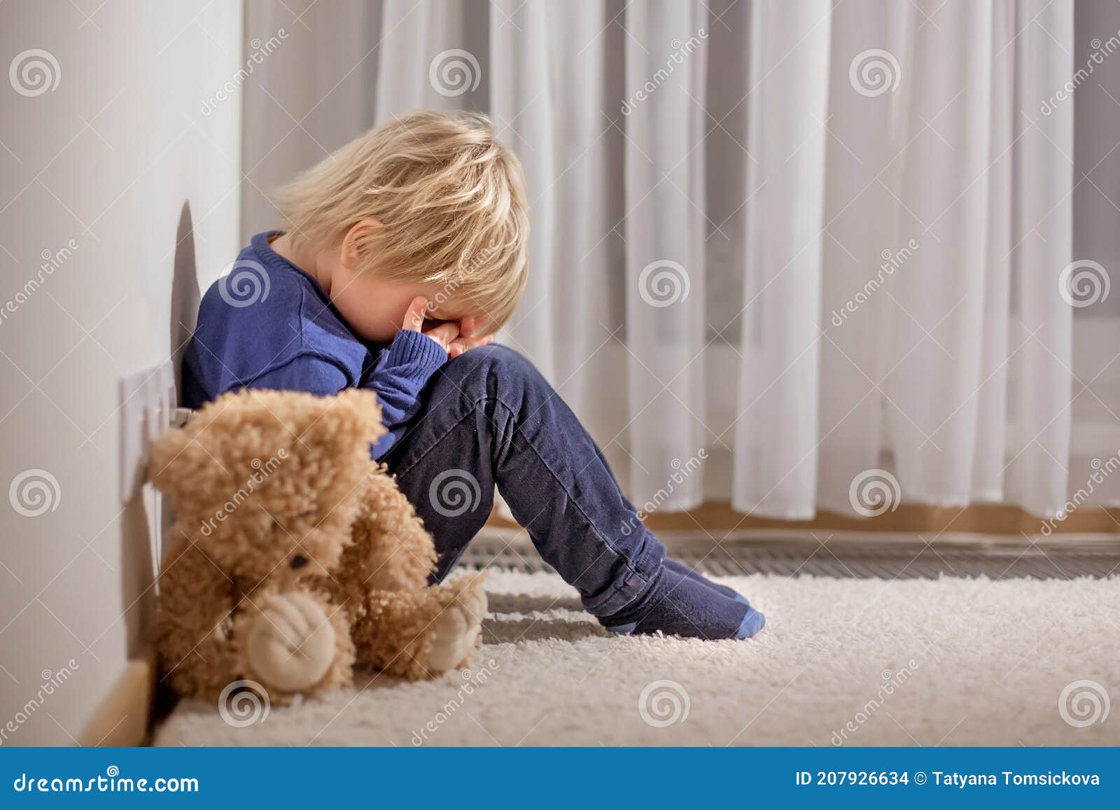sad little toddler child, blond boy, sitting in corner with teddy punished for mischief
