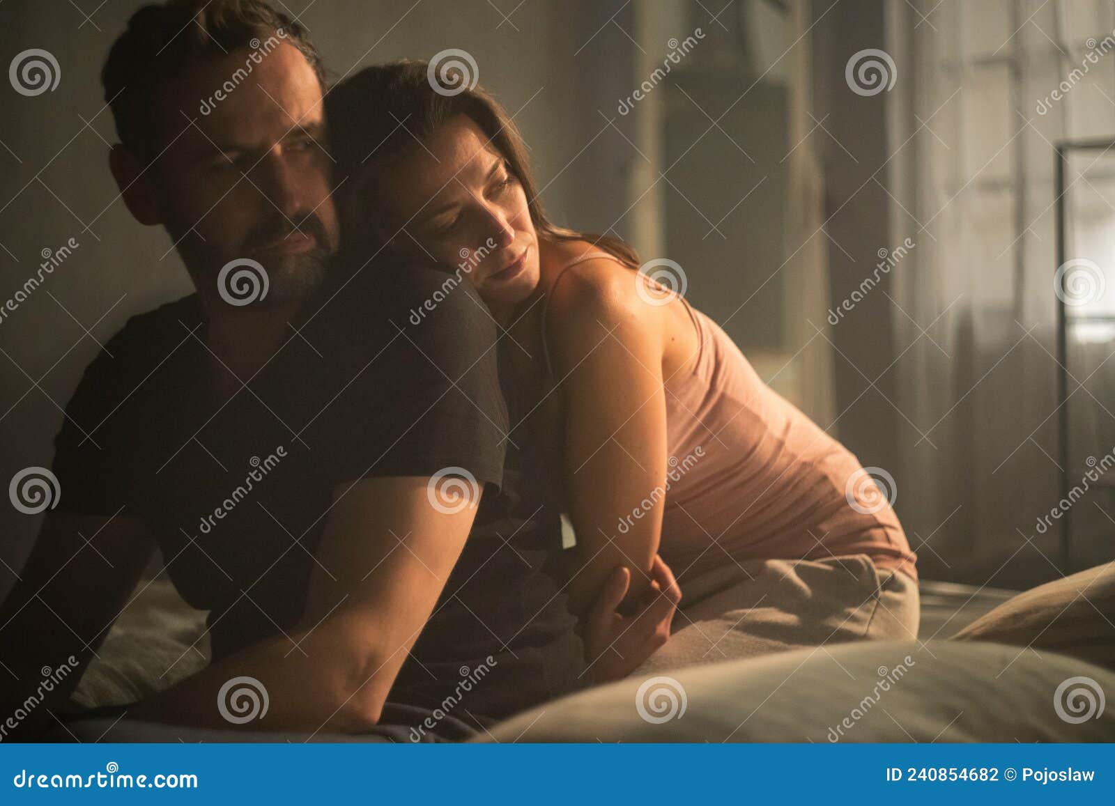 Sad Mature Man is Looking Down, Thinking about Cheating His Wife, while His Wife is Snuggling To Him Stock Photo image