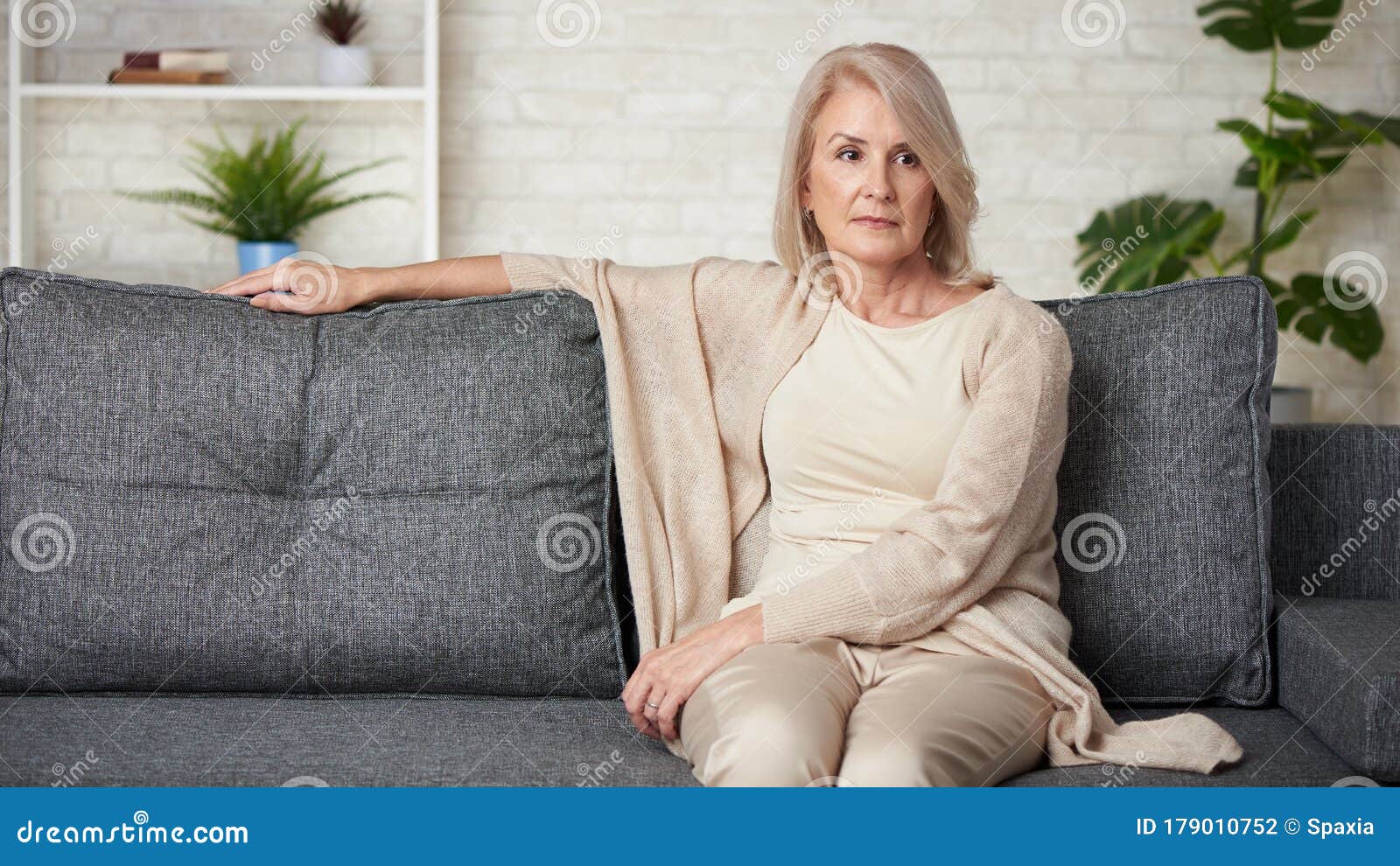 sad older woman is sitting on a sofa at home