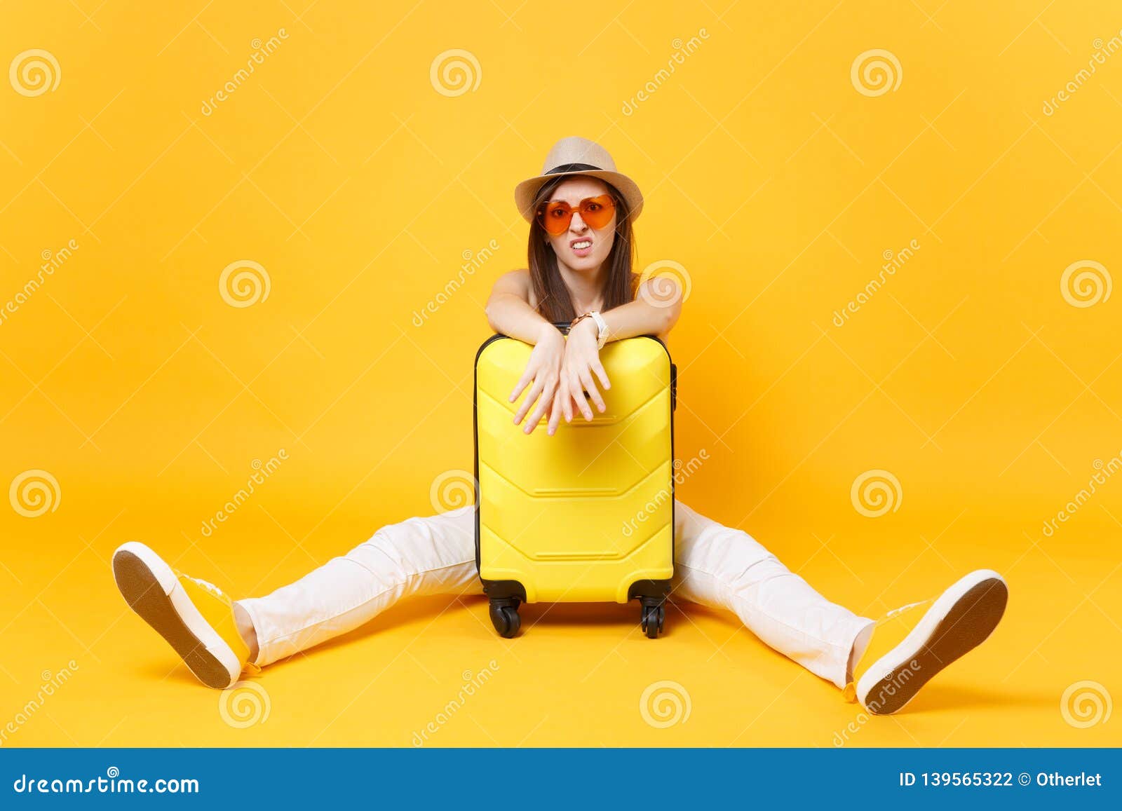 sad traveler tourist woman in summer casual clothes, hat sit near suitcase on yellow orange background. female