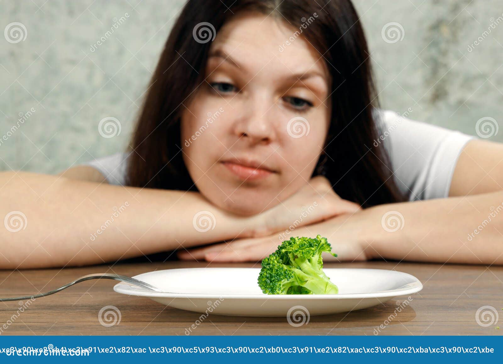 sad young brunette woman dealing with anorexia nervosa or bulimia having small green vegetable on plate. dieting problems, eating