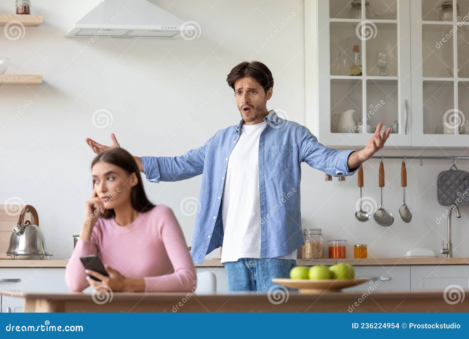 sad young european woman with smartphone ignores offended angry screaming gesticulating husband