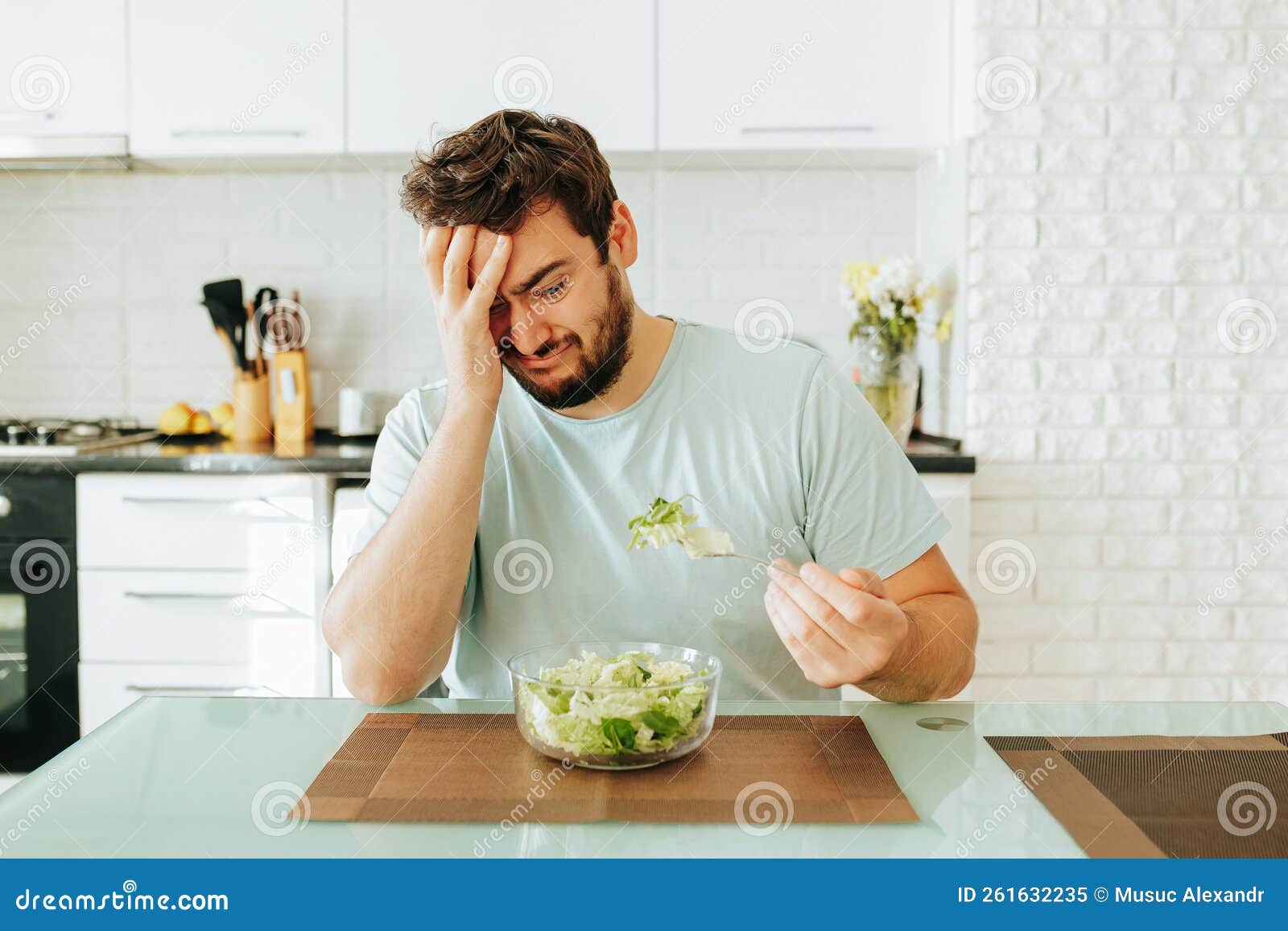 sad young man look longingly at salad hold fork with greens in hand plate salad in front of him.