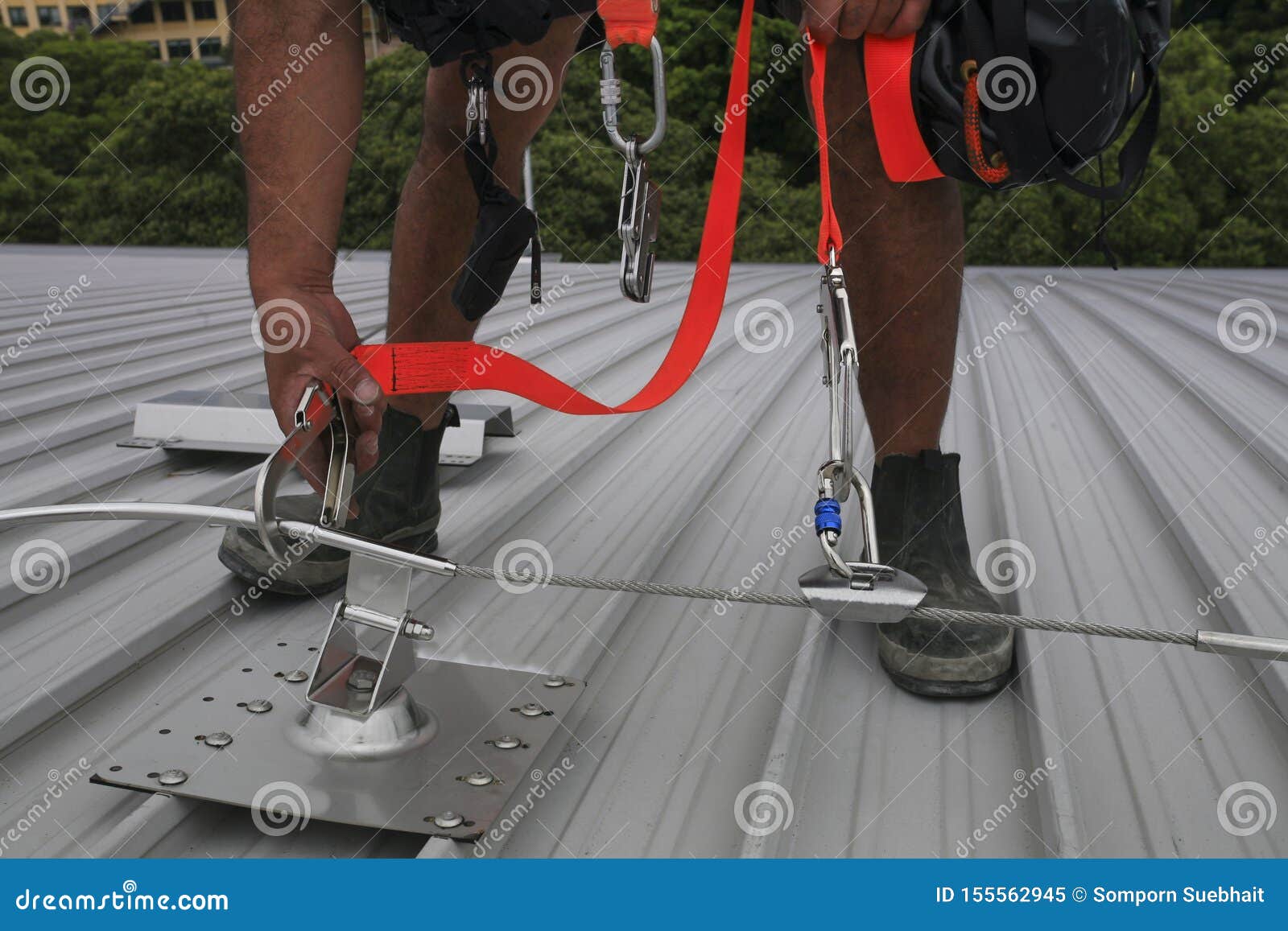 trained worker clipping stainless industrial locking hook into fall arrest roof anchor point systems