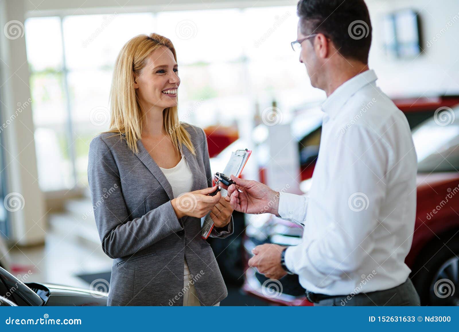 professional salesperson during work with customer at car dealership. giving keys to new car owner.