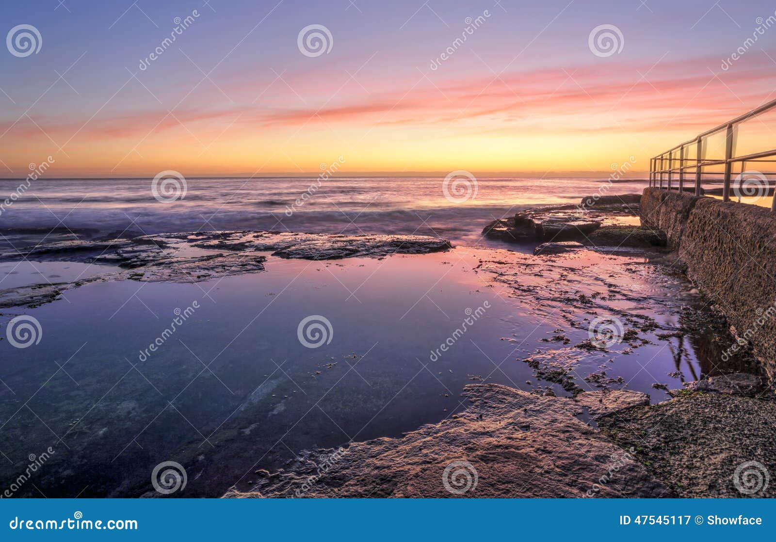 Salida del sol en Wombarra. Las pequeñas ondas se estrellan sobre las repisas de la roca que rodean la piscina del océano en Wombarra NSW Australia