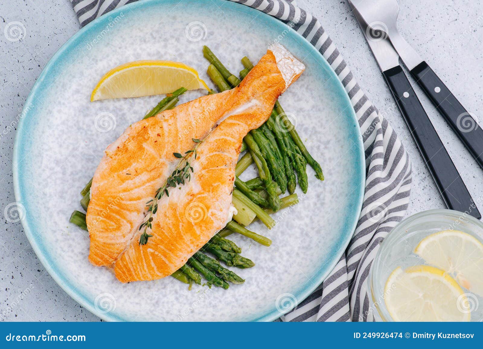 salmon placed on fried asparagus on a plate with lemon slice.