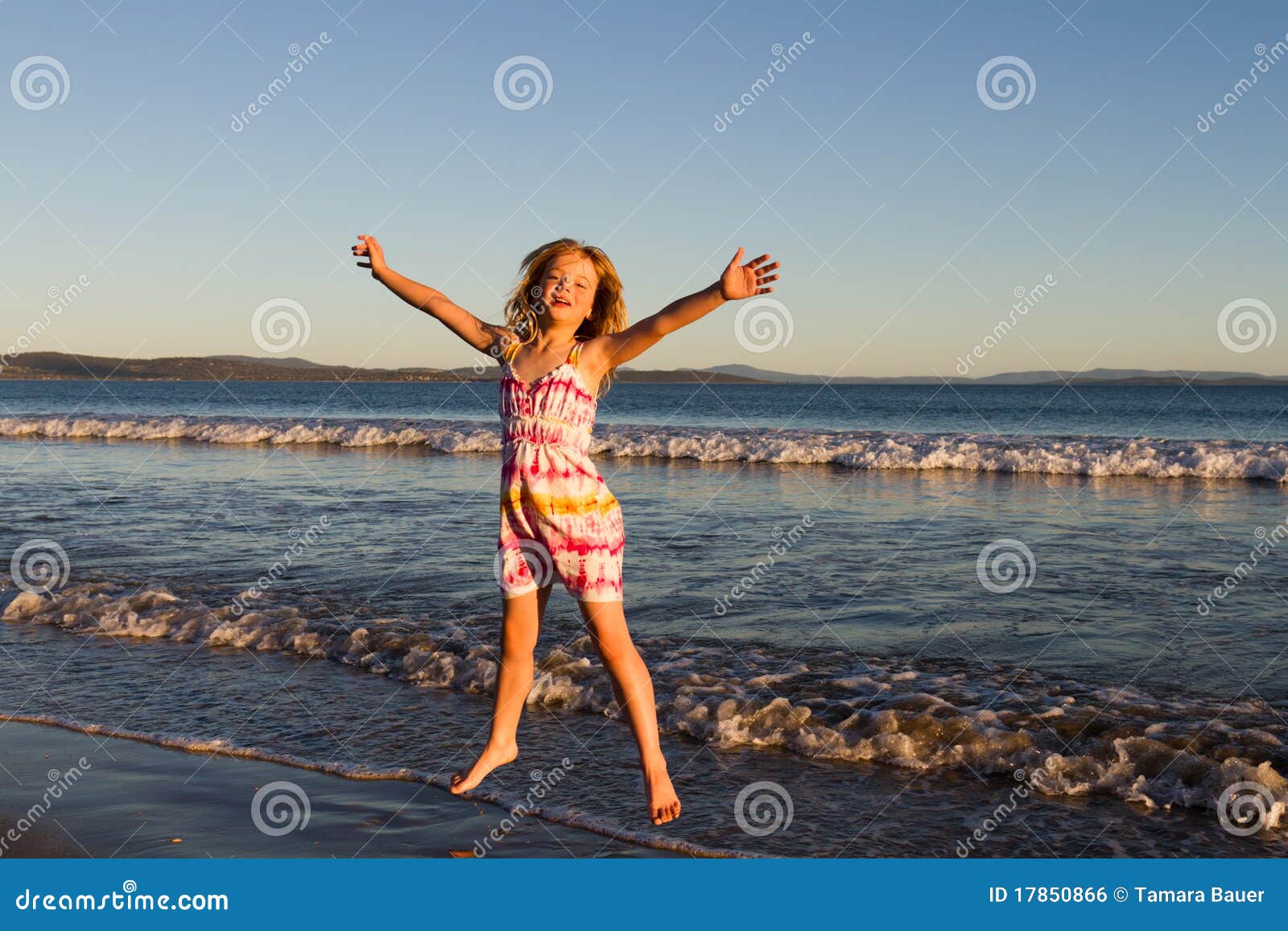 Salto para a alegria. Menina encantadora em um vestido que salta para a alegria nas ondas na praia.