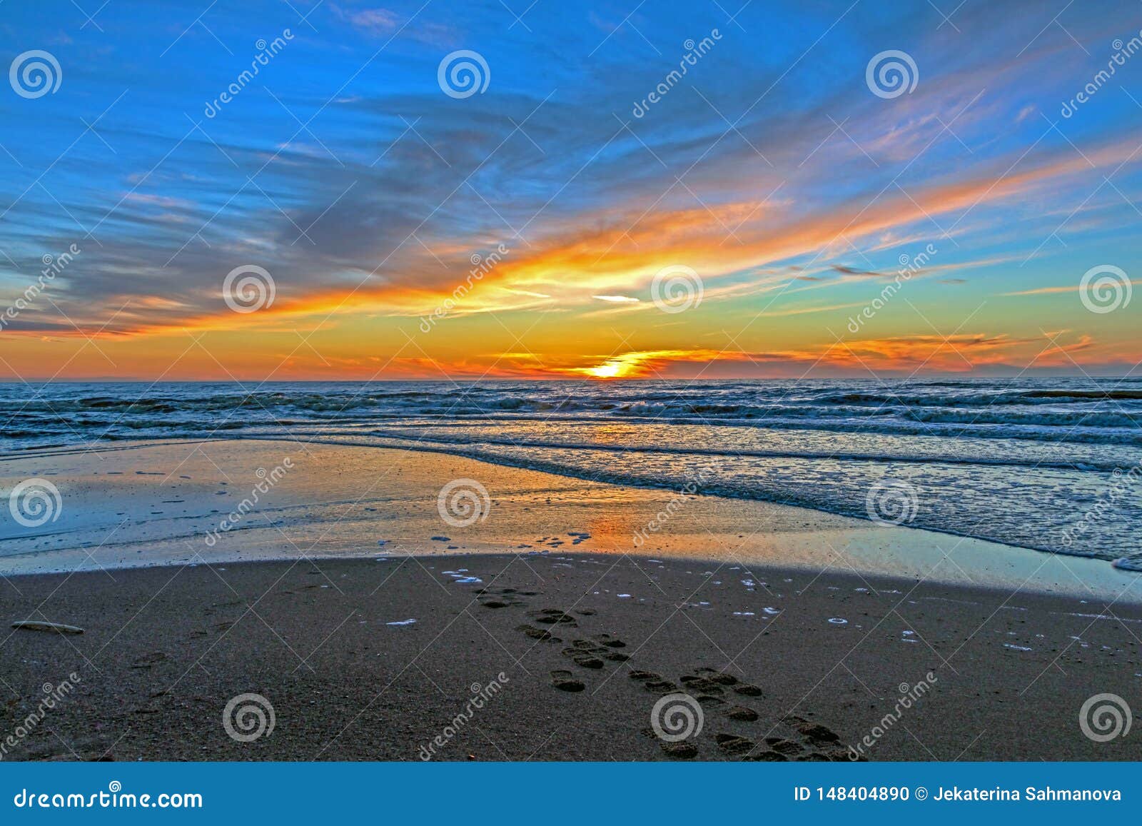 sand beach with endless horizon and foamy waves under the bright sundown with yellow colors and clouds above the sea
