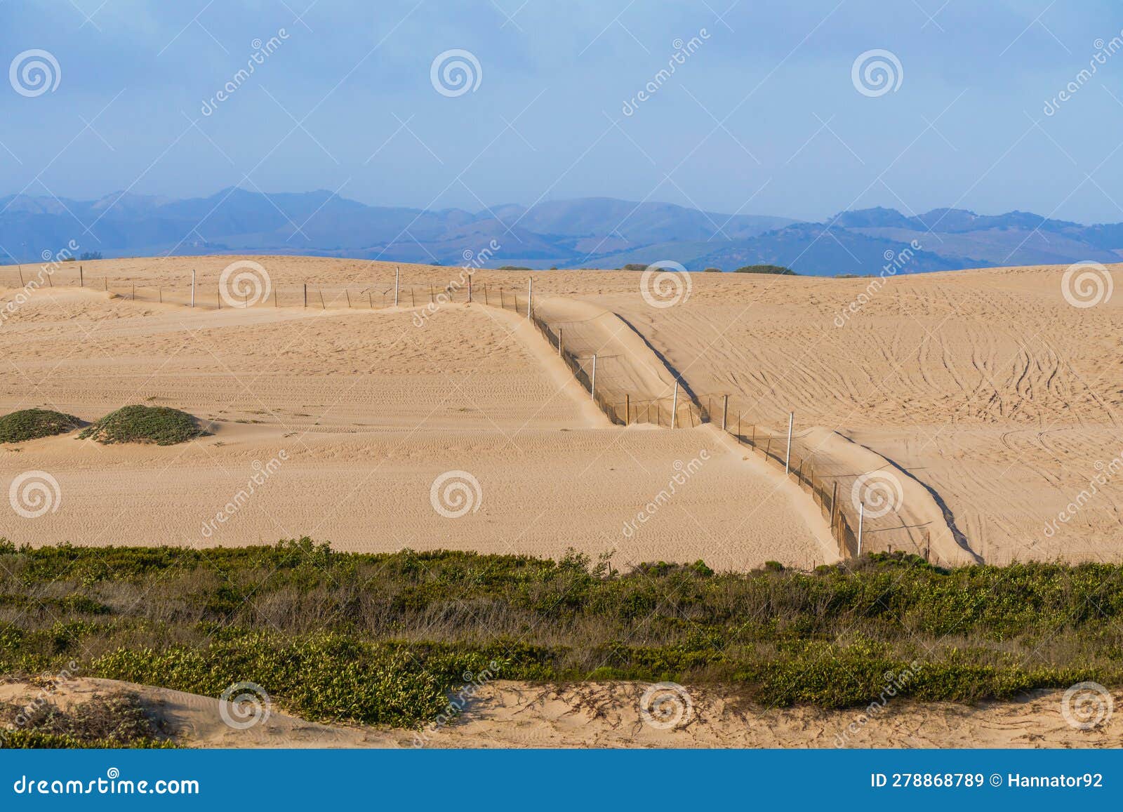sand dunes, silhouettes of mountains, and a cloudy sky in the background. oceano dunes, california