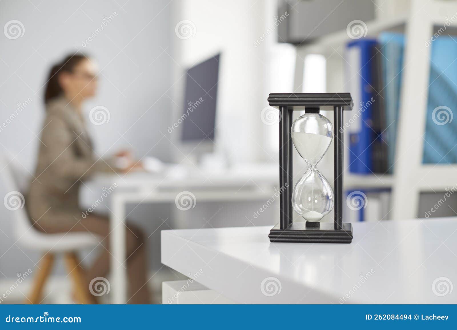 sandglass at desk on office blur background with woman working on computer.