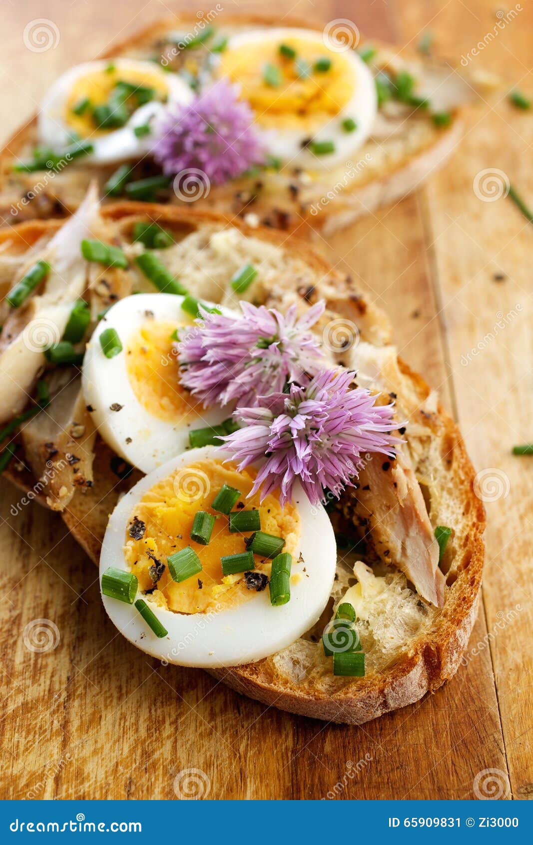 sandwich with adition of mackerel fish , eggs and edible flowers of chives on wooden table