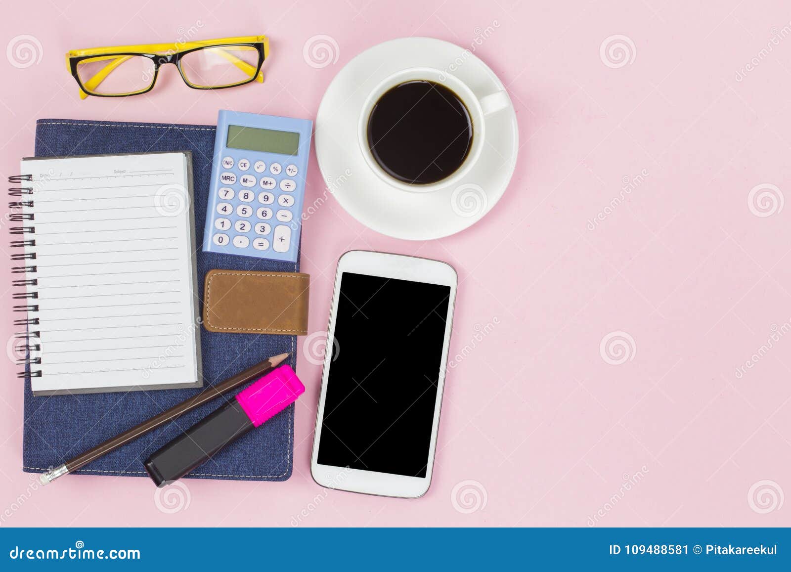 A sarja de Nimes azul da tampa do caderno com a calculadora móvel da etiqueta vazia e o copo branco do café preto amarelam vidros no estilo pastel do fundo cor-de-rosa com o copyspace flatlay