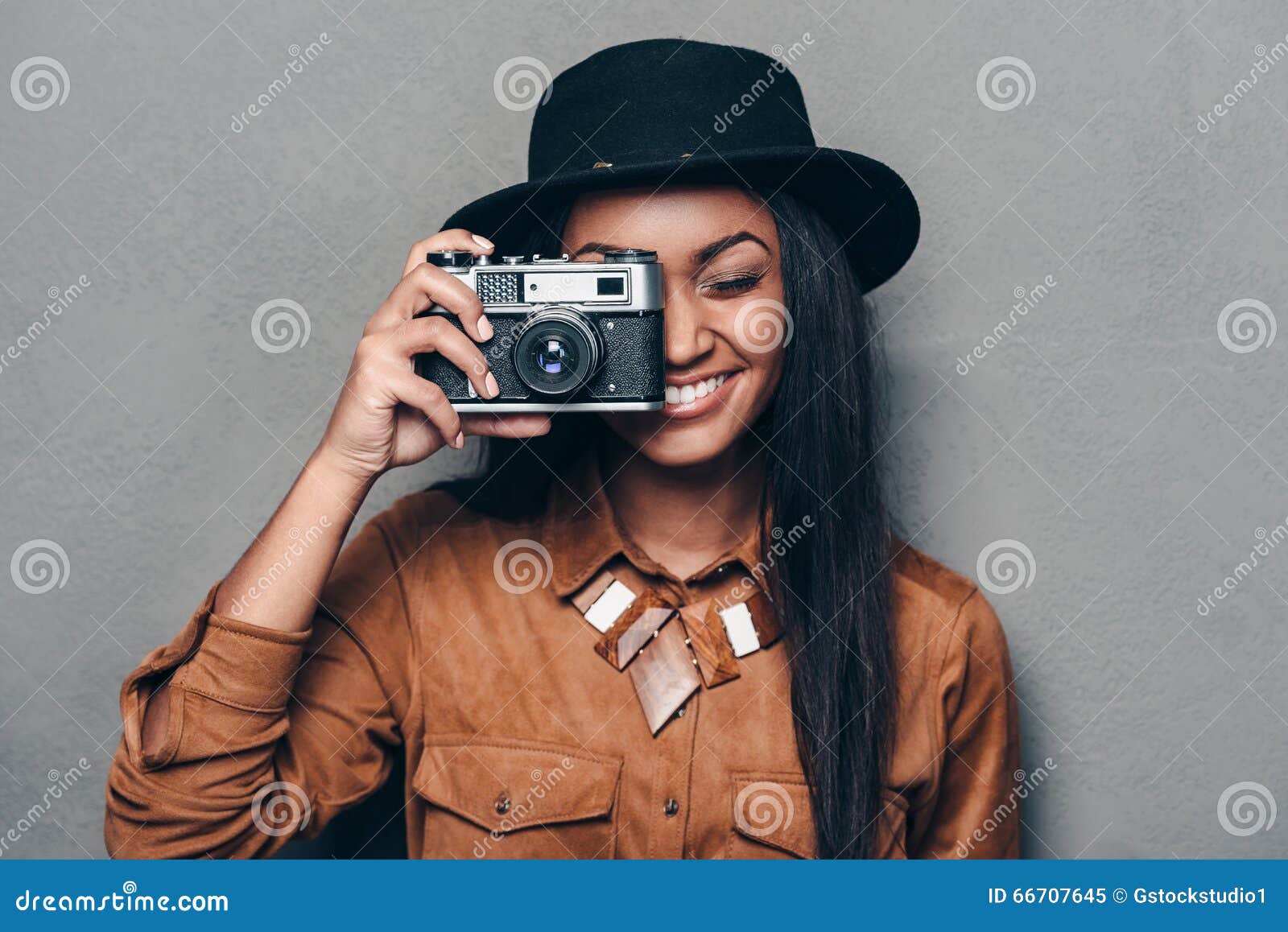 Say cheese!. Beautiful cheerful young African woman holding retro styled camera and focusing on you with smile while standing against grey background