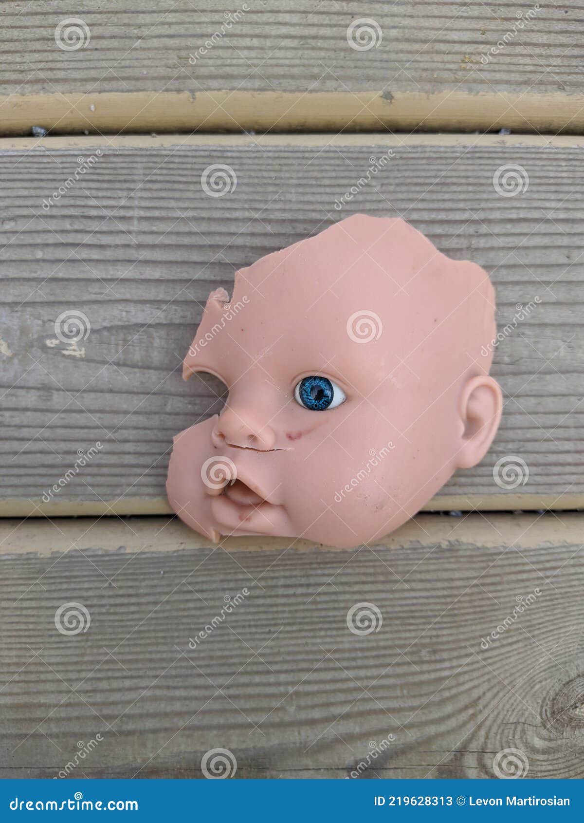 scary and broken doll face with one blue eye on a background of gray wooden background