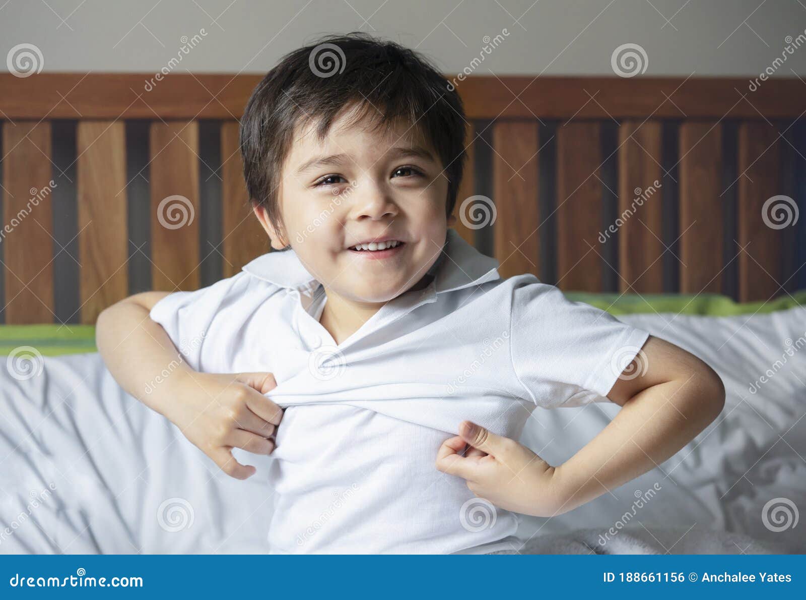 school boy sitting in bed and try to wearing his cloth with smiling face,cute kid boy getting dressed and get ready for school,