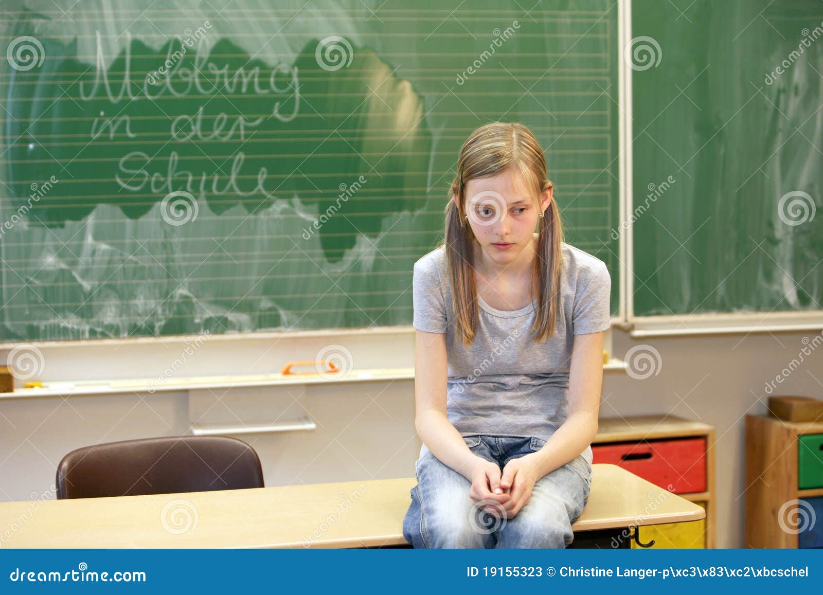 School bullying - horizontal. A sad girl sitting in the classroom at school in front of a blackboard with the words bullying at school