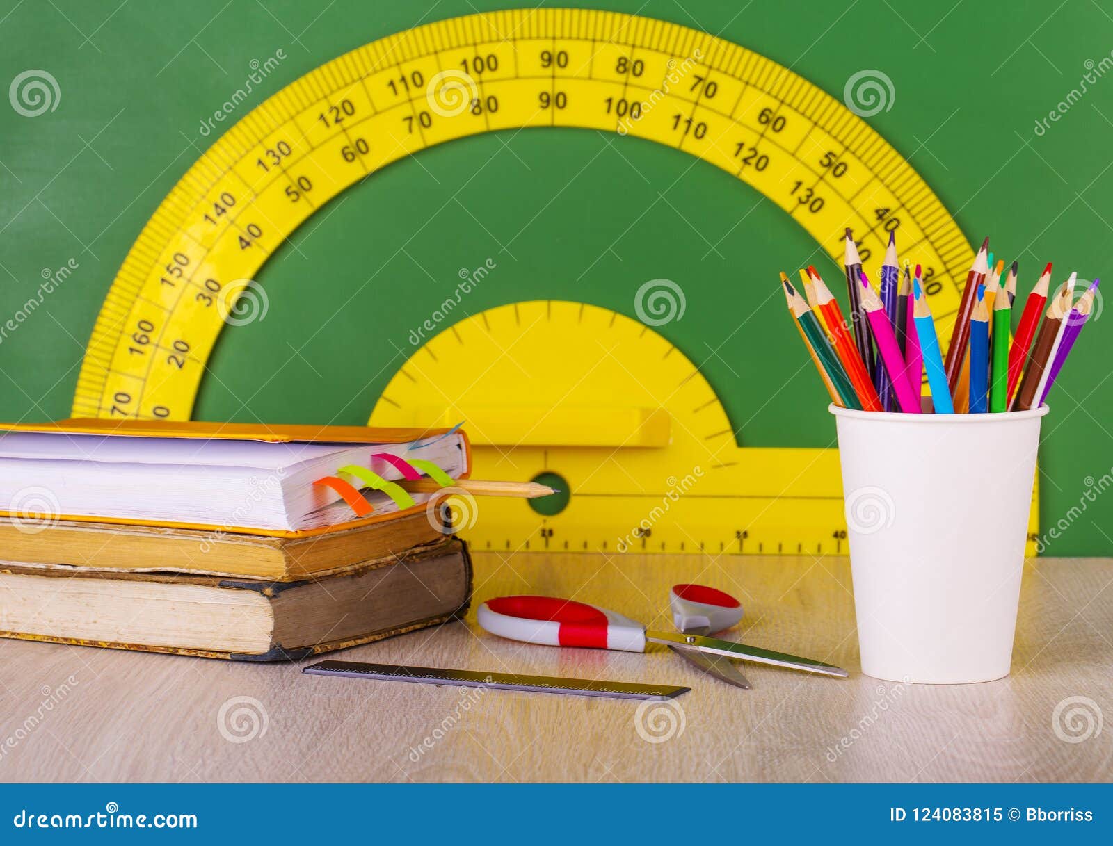 school concept: colore pencil, book, ruler, scissors and green chalkboard with yellow protractor.
