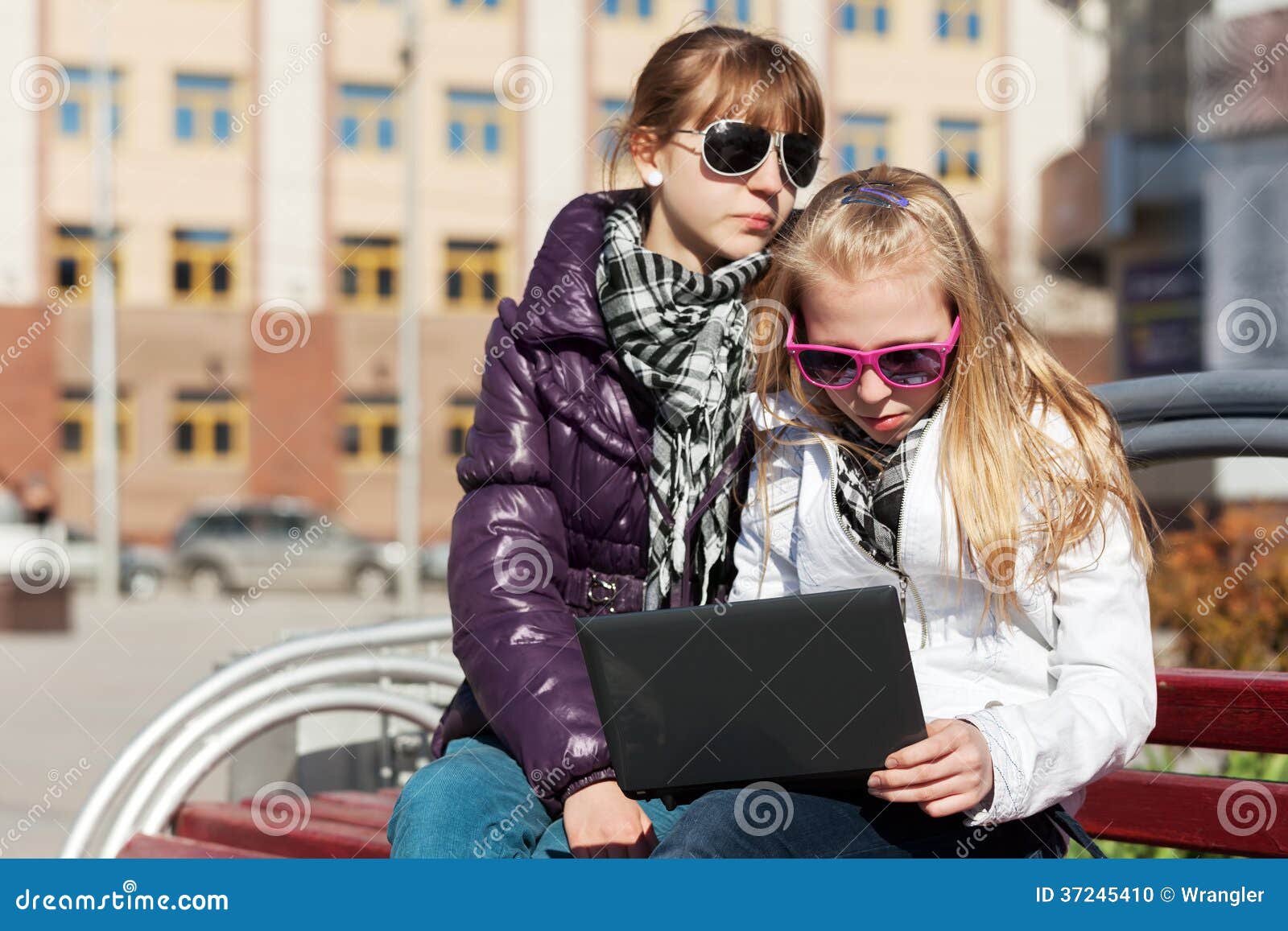 School girls using laptop on the bench. Teenage schoolgirls using laptop on the bench