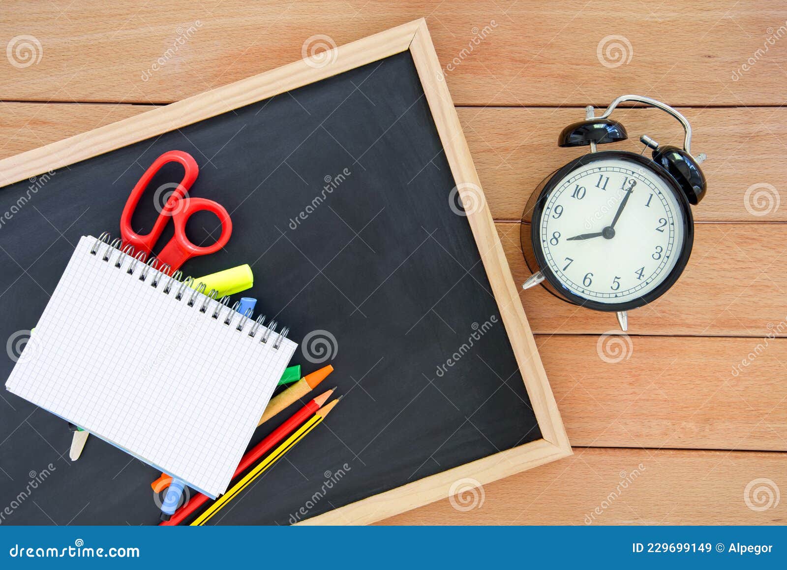 school supplies on ablackboard lying on a table next to an alarma clock