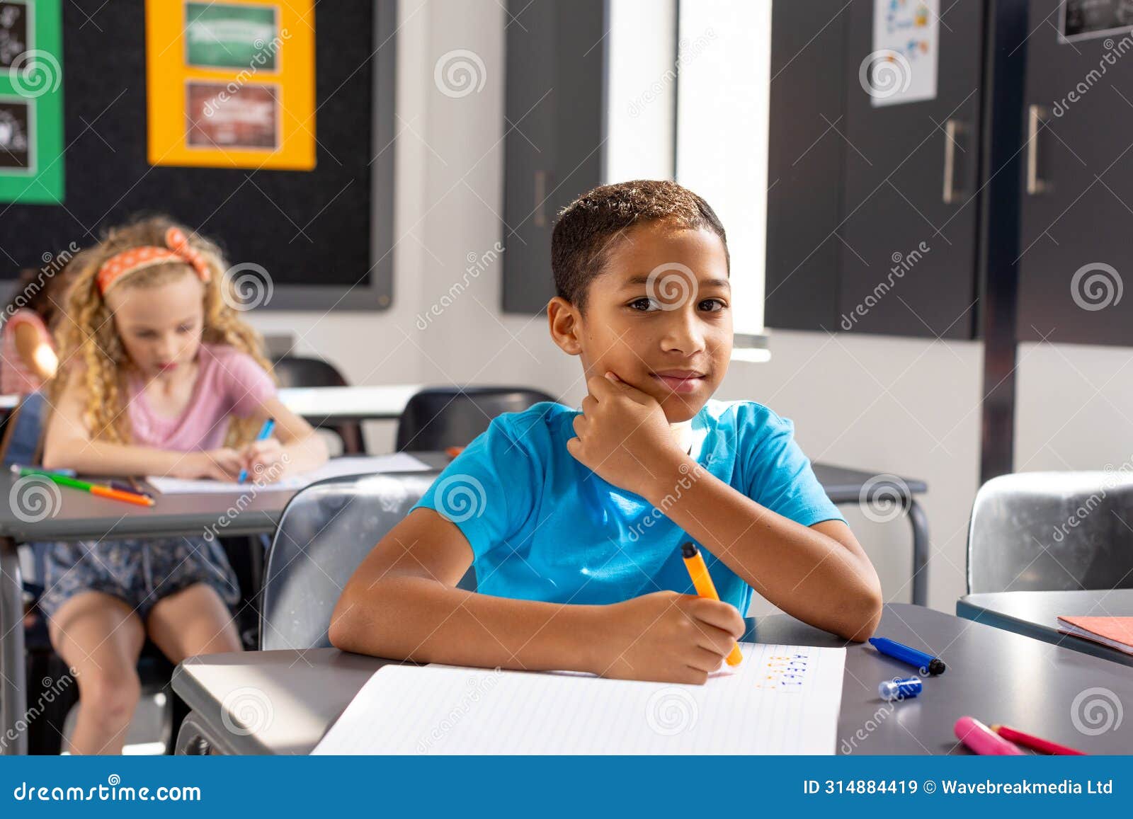 in school, young biracial male student sitting at a desk in a classroom, looking thoughtful