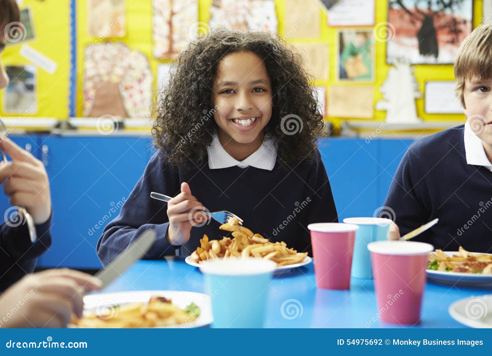 schoolchildren sitting at table eating cooked lunch