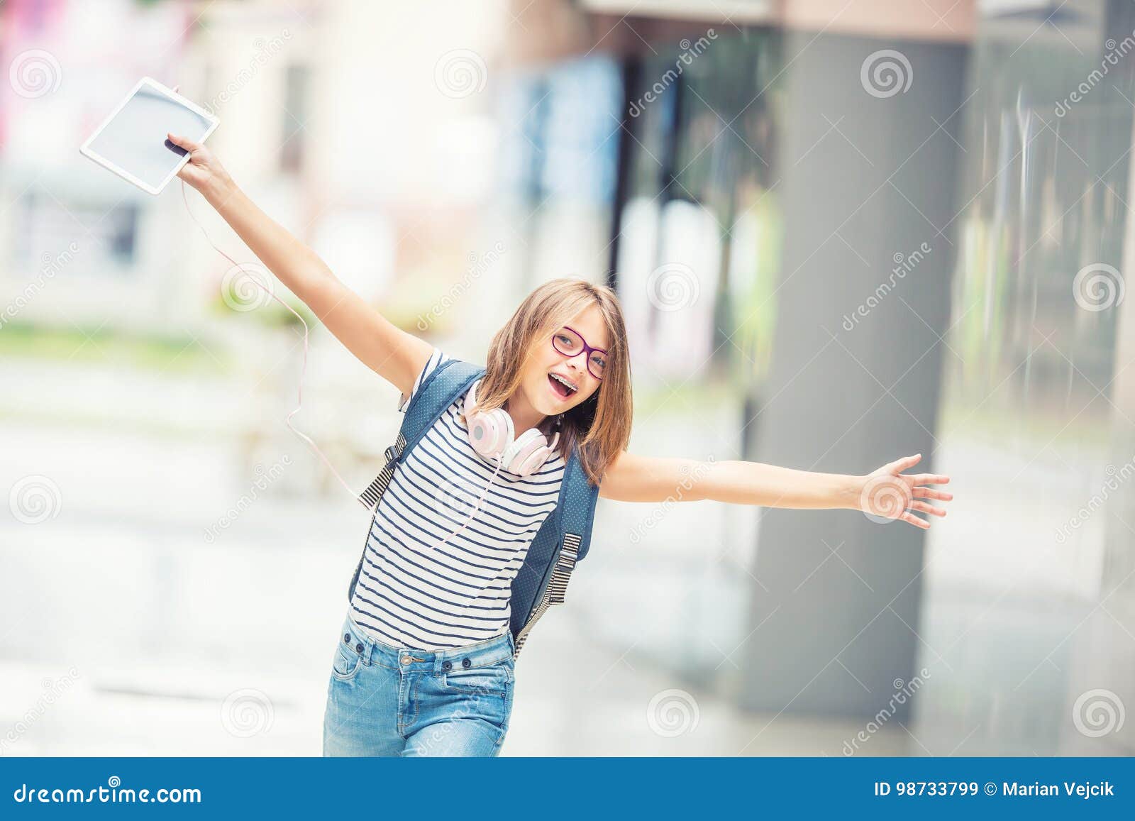 Schoolgirl with bag, backpack. Portrait of modern happy teen school girl with bag backpack headphones and tablet. Girl with dental braces and glasses.