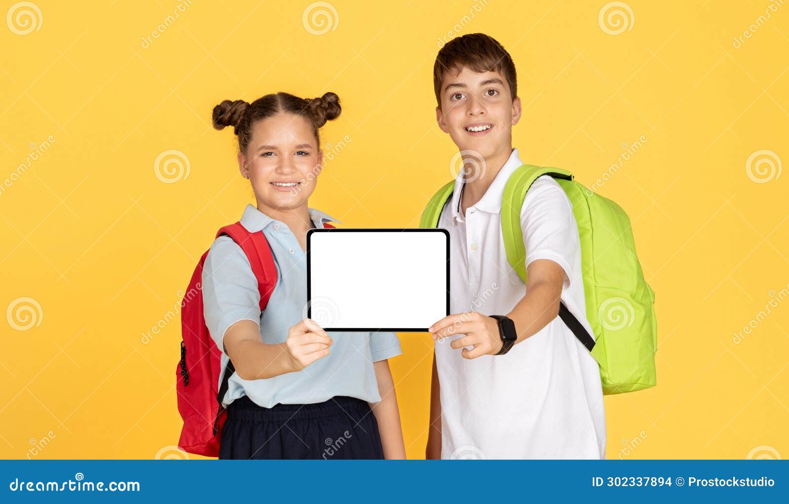 a schoolgirl and schoolboy with backpacks smilingly present a tablet with a white screen